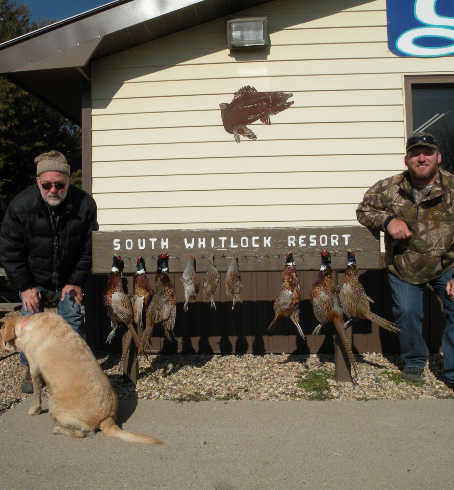 Two men and a dog standing in front of a sign that says south whitlock resort