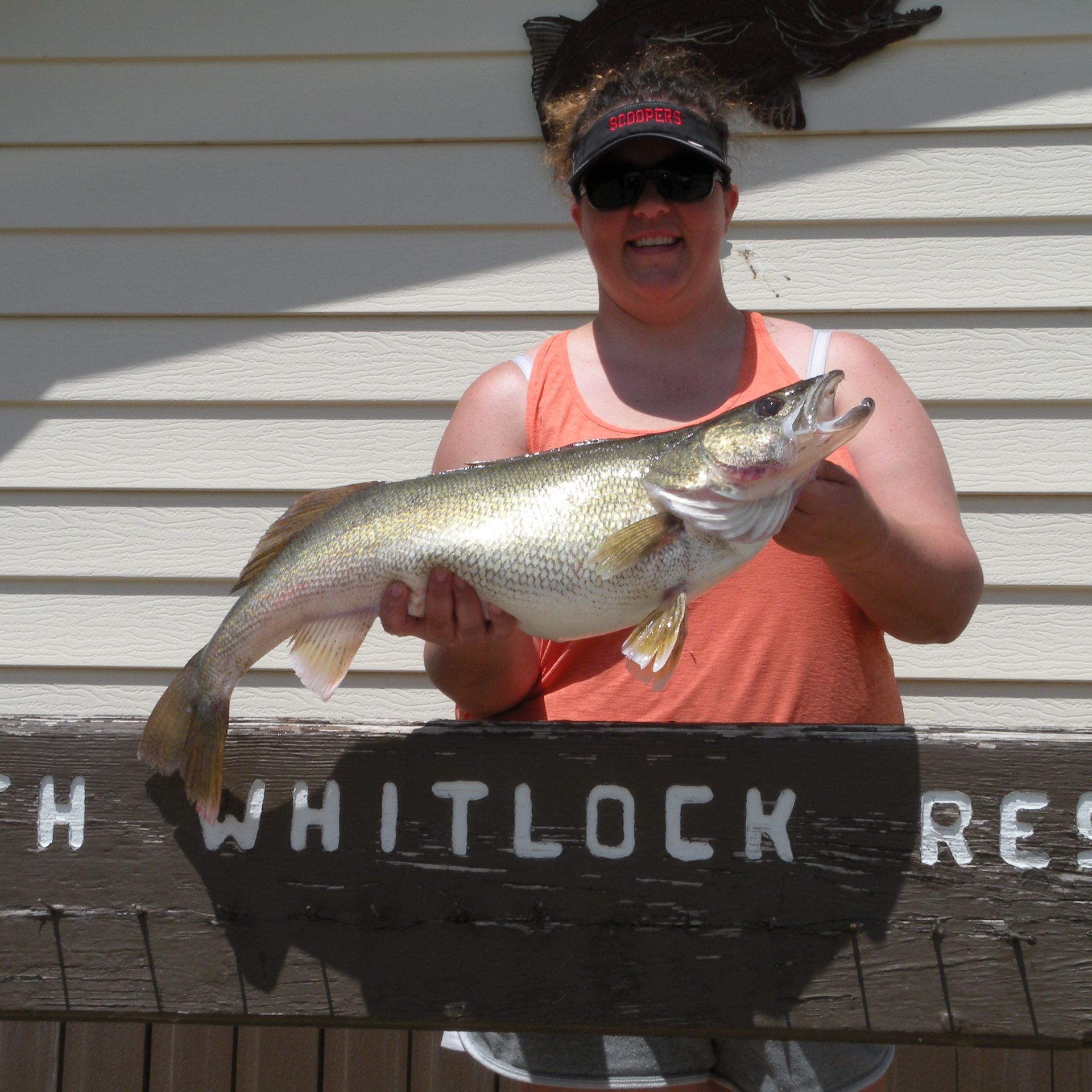 A woman holding a large fish in front of a sign that says whitlock