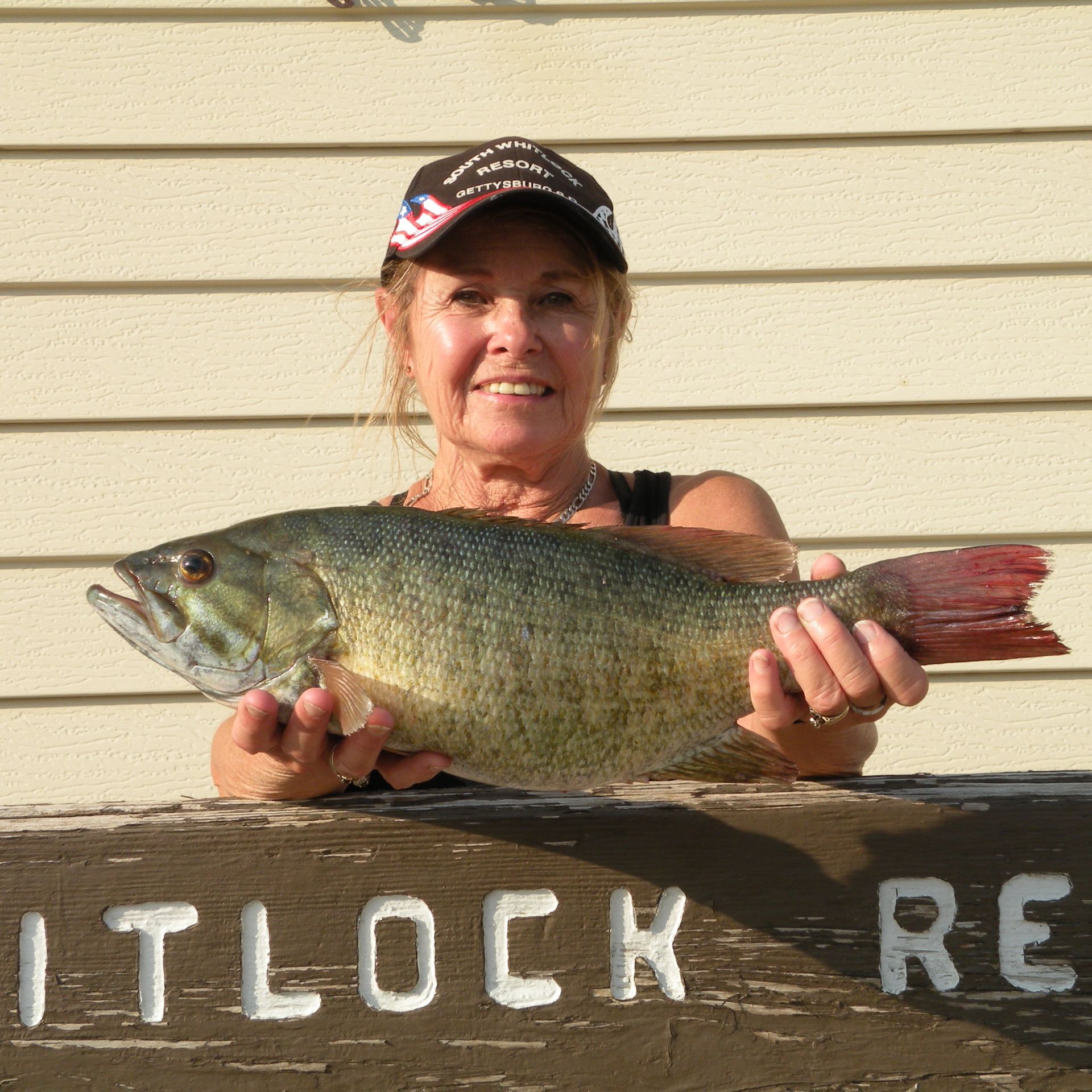 A woman is holding a large fish in front of a sign that says itlock re