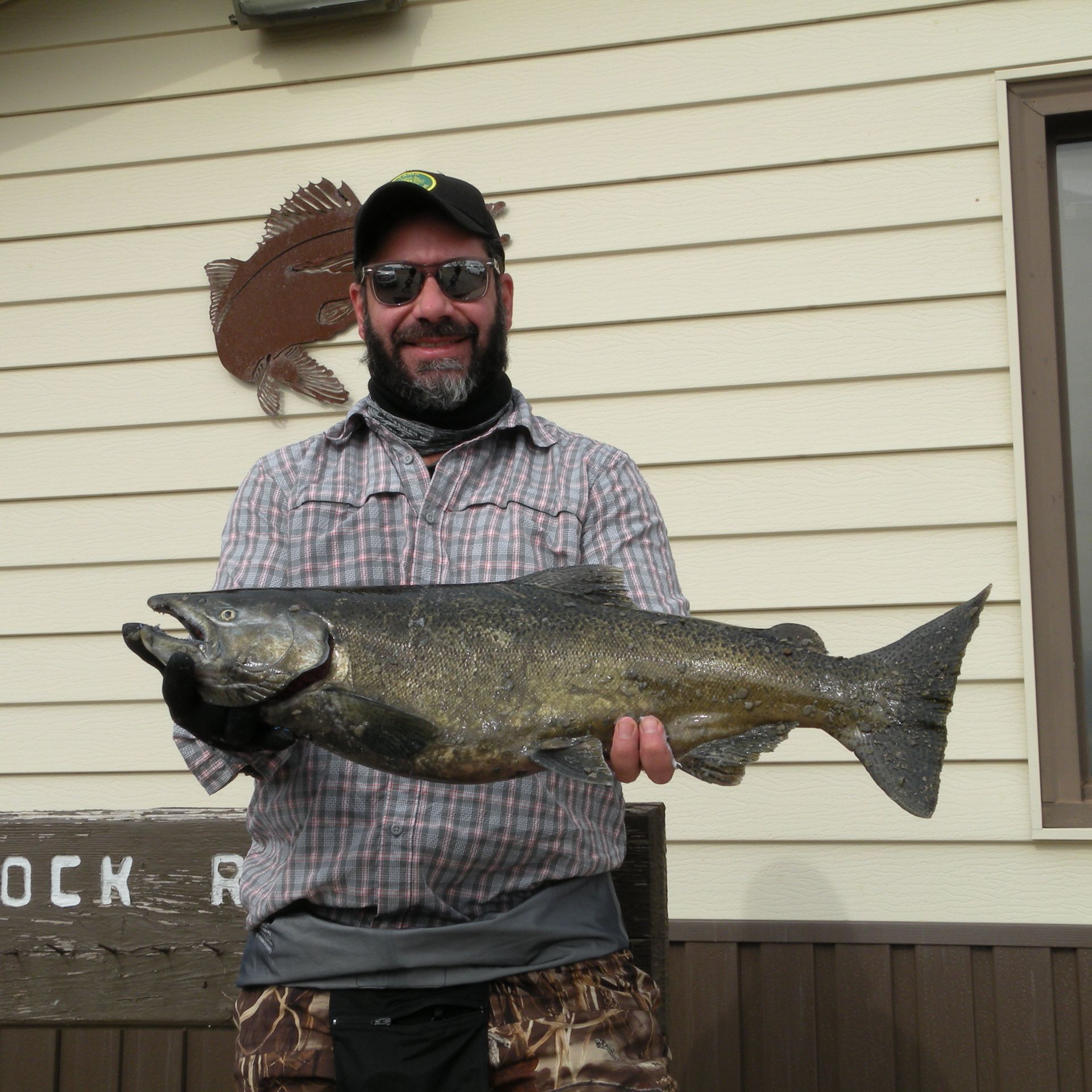 A man holding a large fish in front of a sign that says buck r
