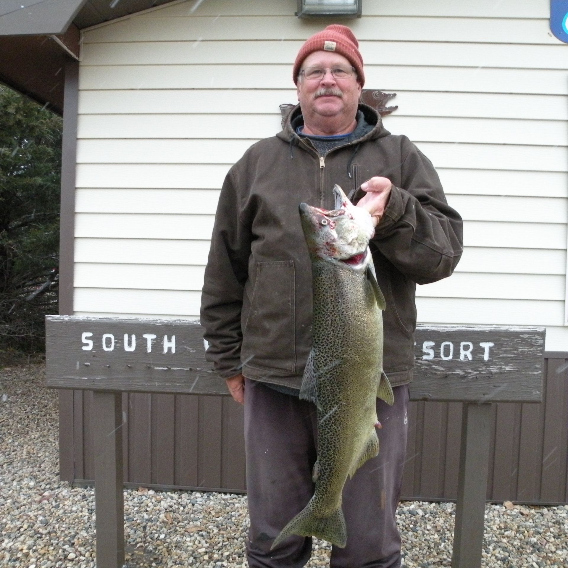 A man holding a large fish in front of a sign that says south sort