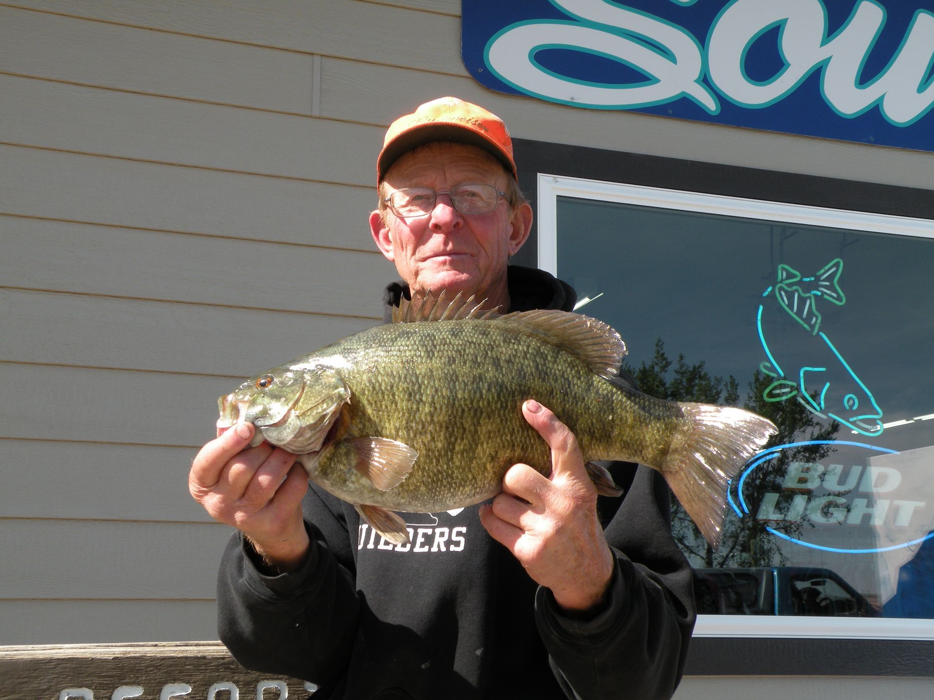 A man is holding a large fish in front of a bud light sign