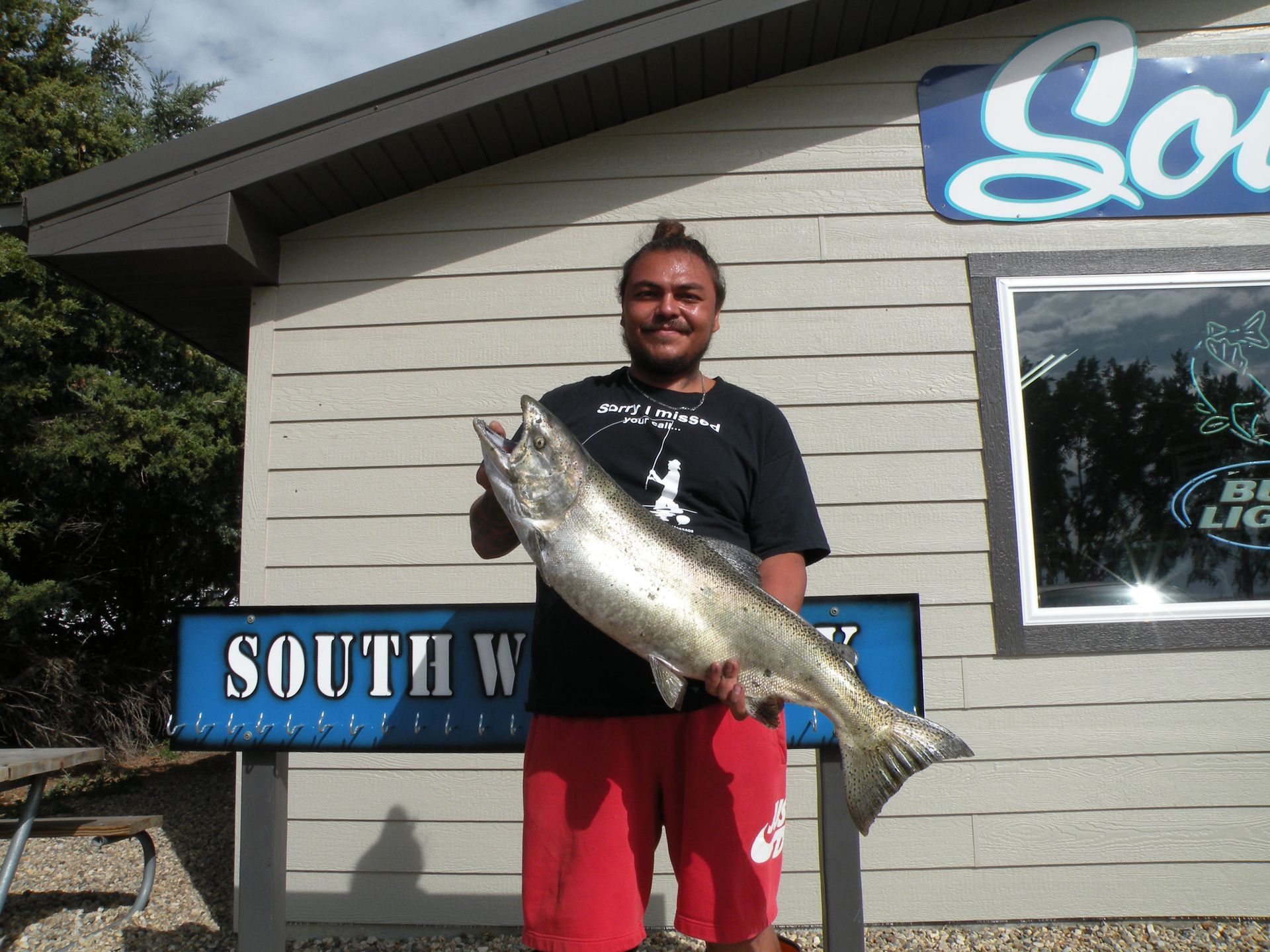 A man holding a large fish in front of a building that says south west