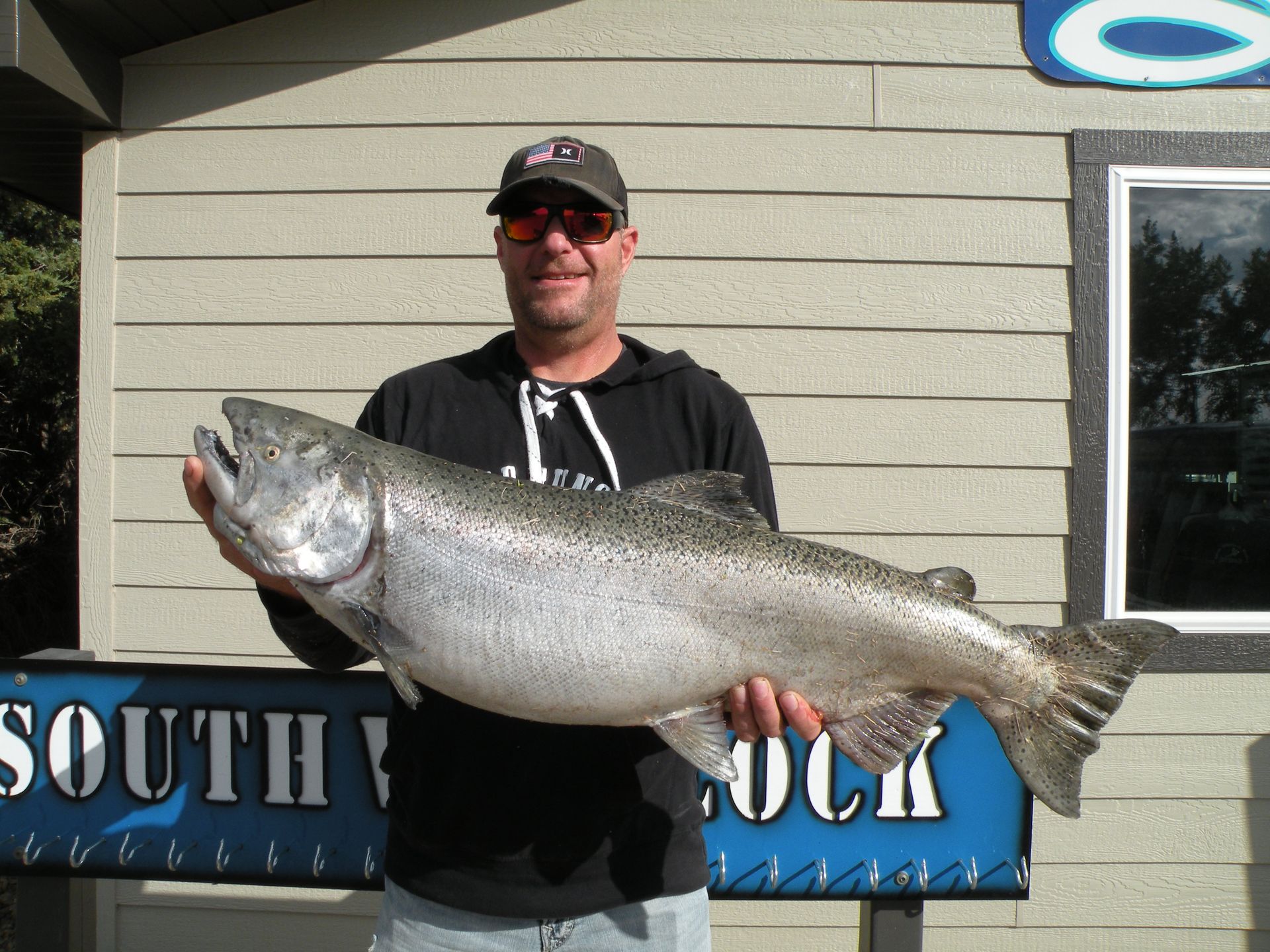 A man is holding a large fish in front of a sign that says south rock