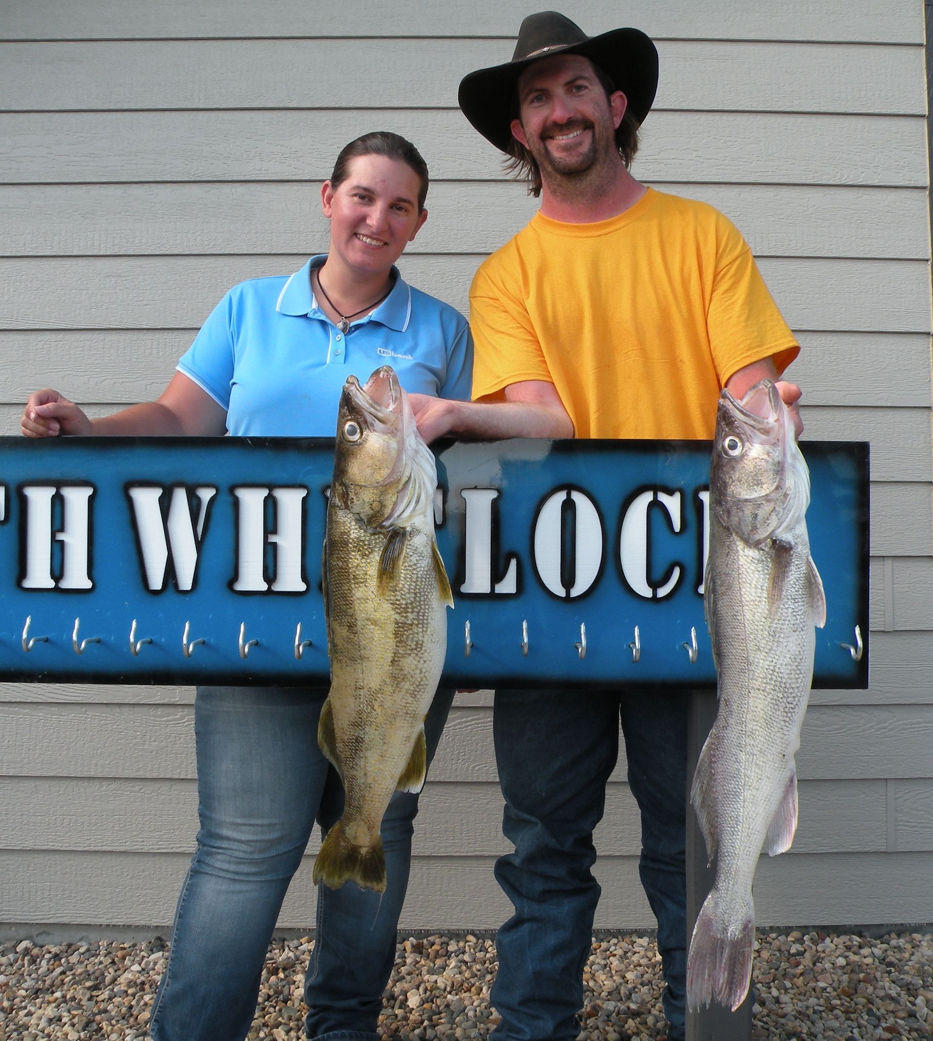 A man and a woman holding fish in front of a sign that says hwh loc