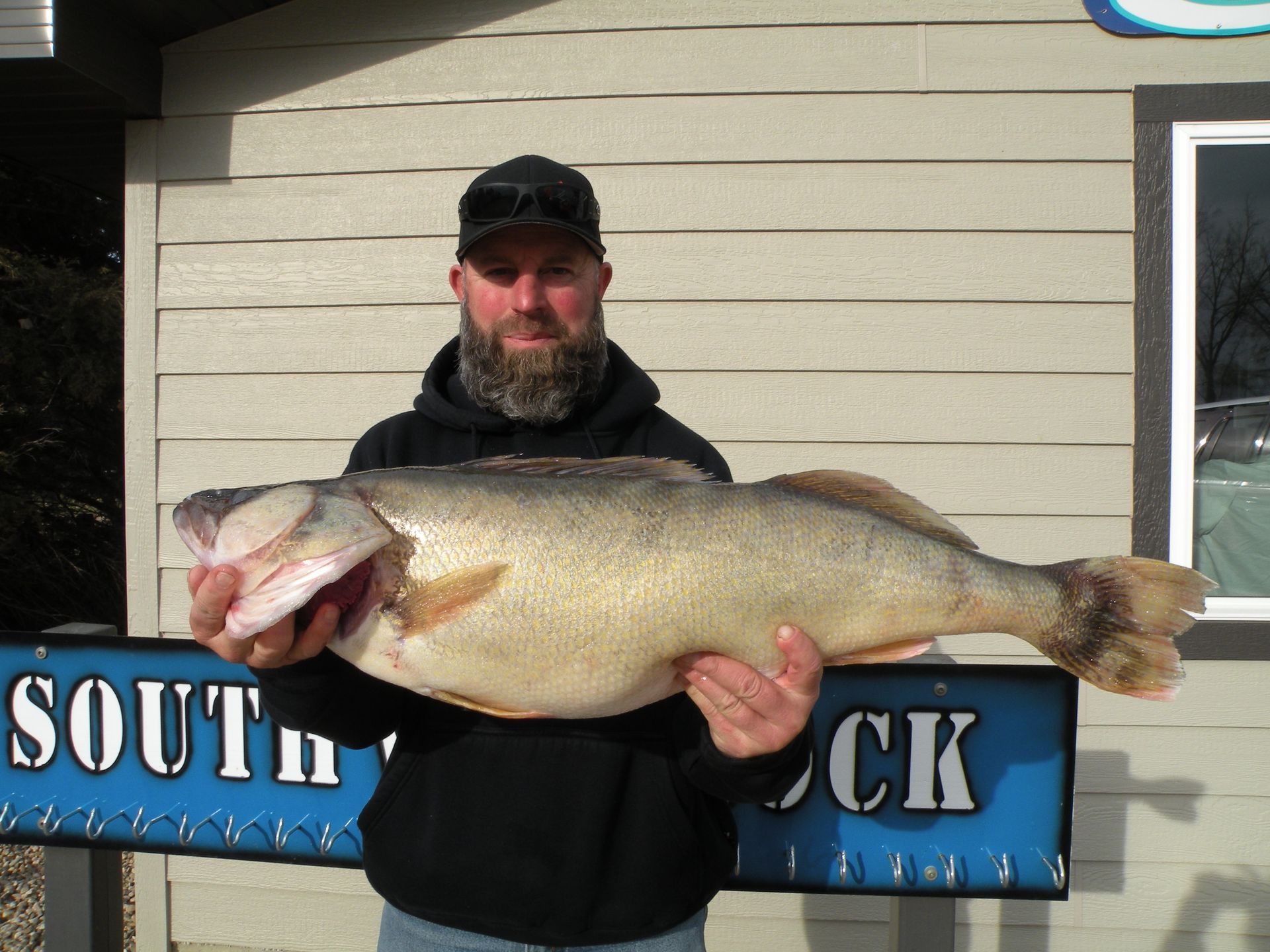 A man is holding a large fish in front of a south dock sign