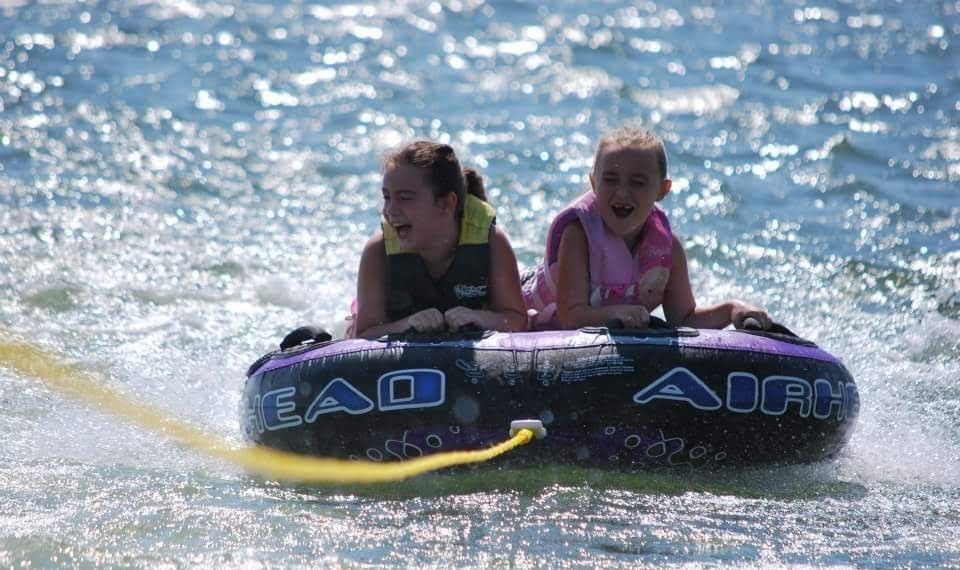 Two young girls are riding a tube in the water.