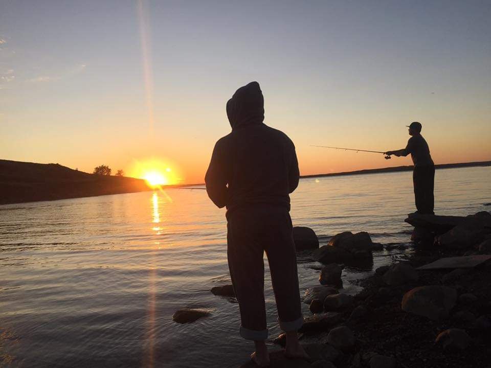 Two people are fishing in the water at sunset