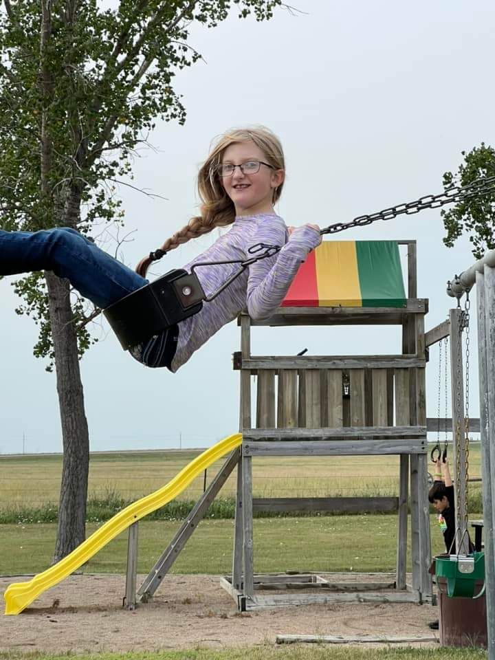 A girl is swinging on a swing set with a yellow slide