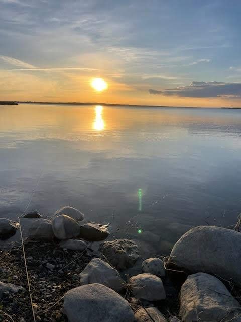 A sunset over a body of water with rocks in the foreground.