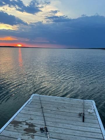 A dock with fishing rods on it overlooking a large body of water at sunset.