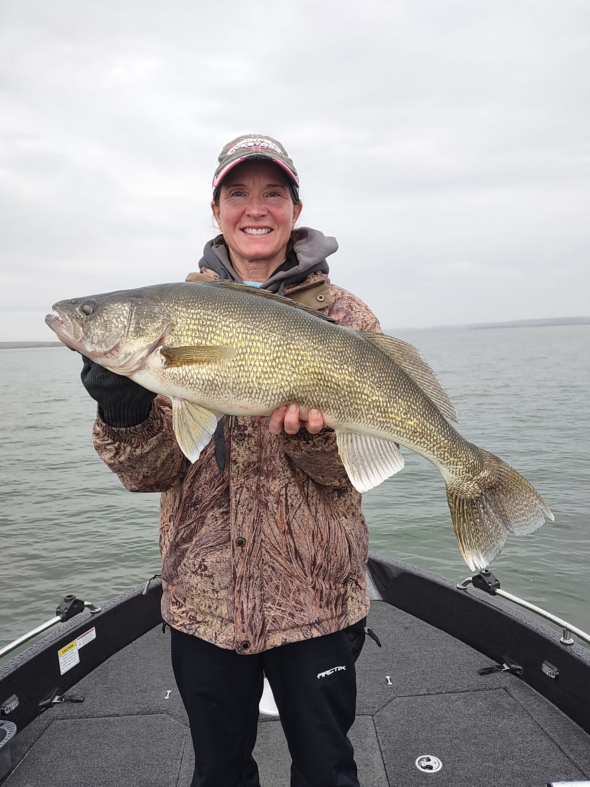 A woman is standing on a boat holding a large fish.