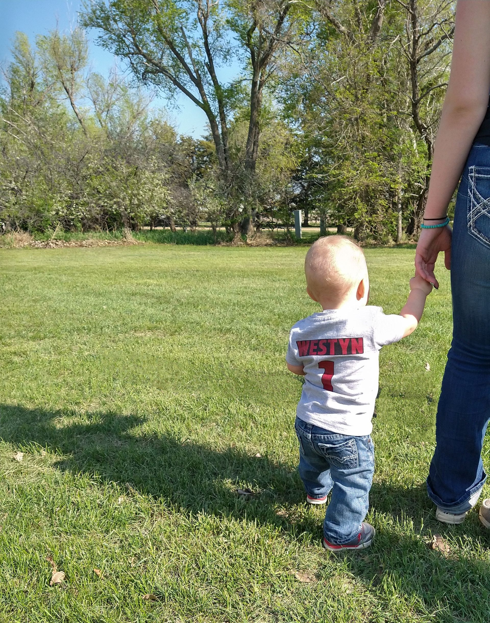 A woman is holding a baby 's hand in a grassy field.