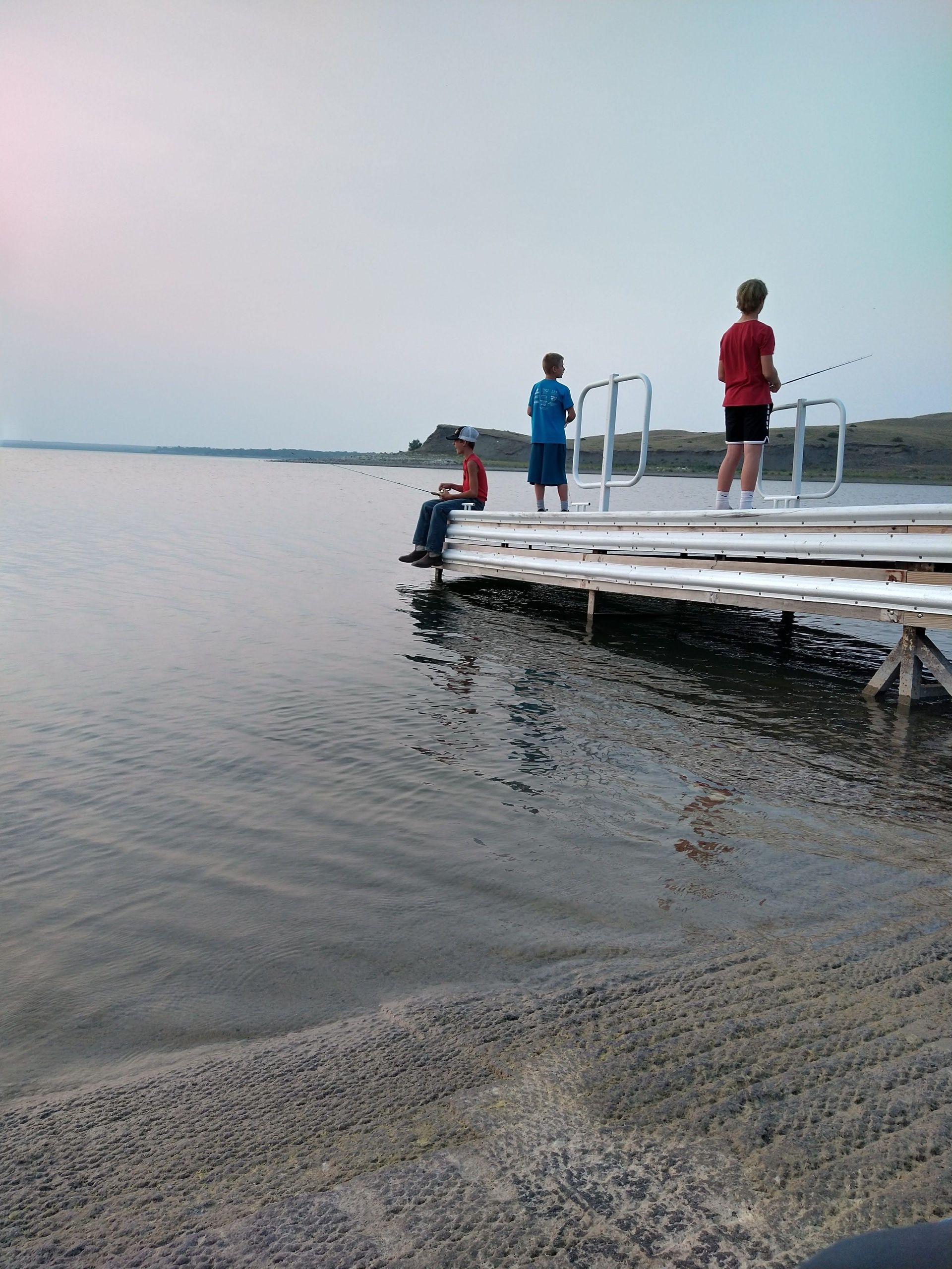 Two boys are fishing on a dock near the water