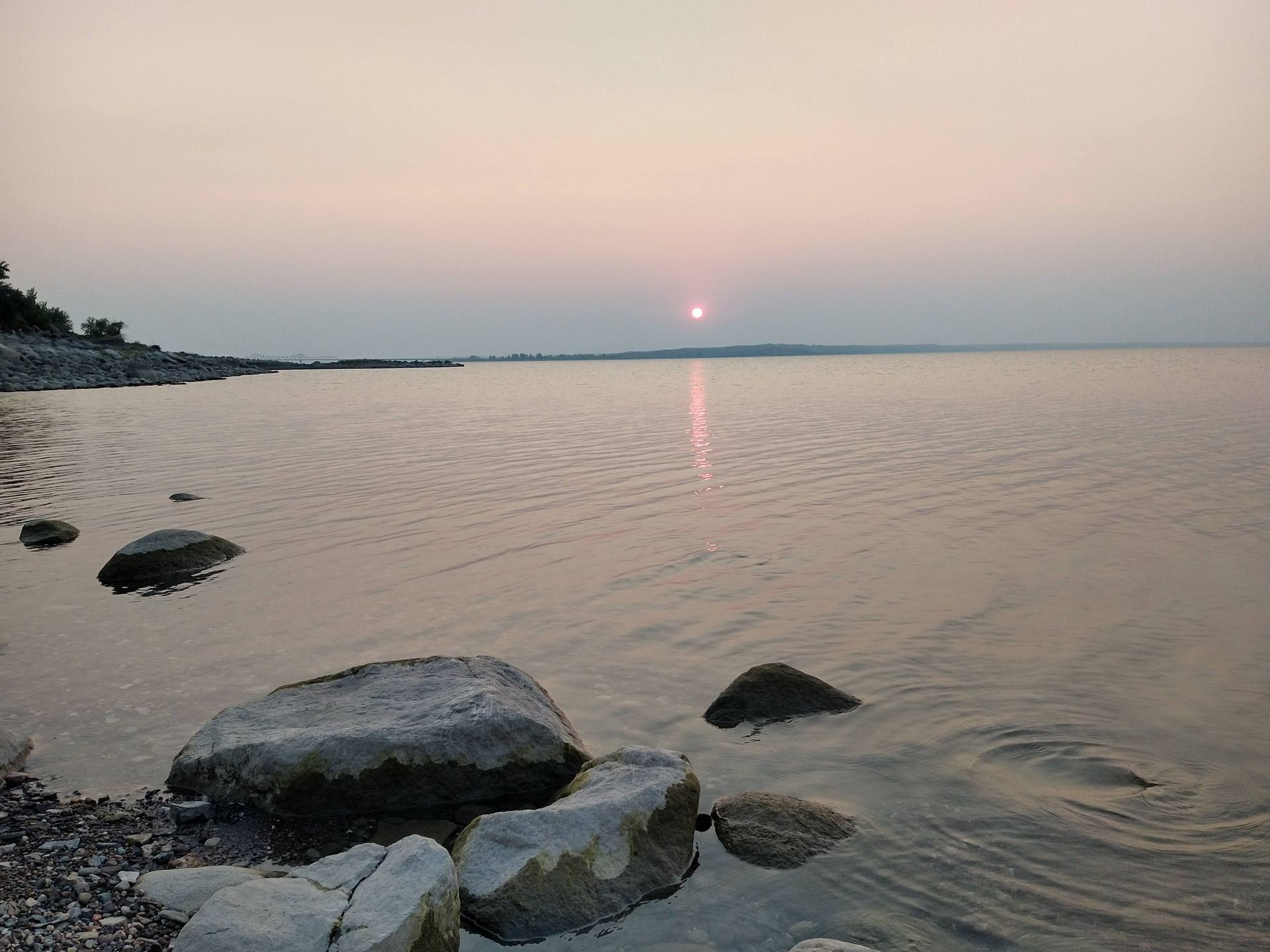 A large body of water with rocks in the foreground and a sunset in the background.