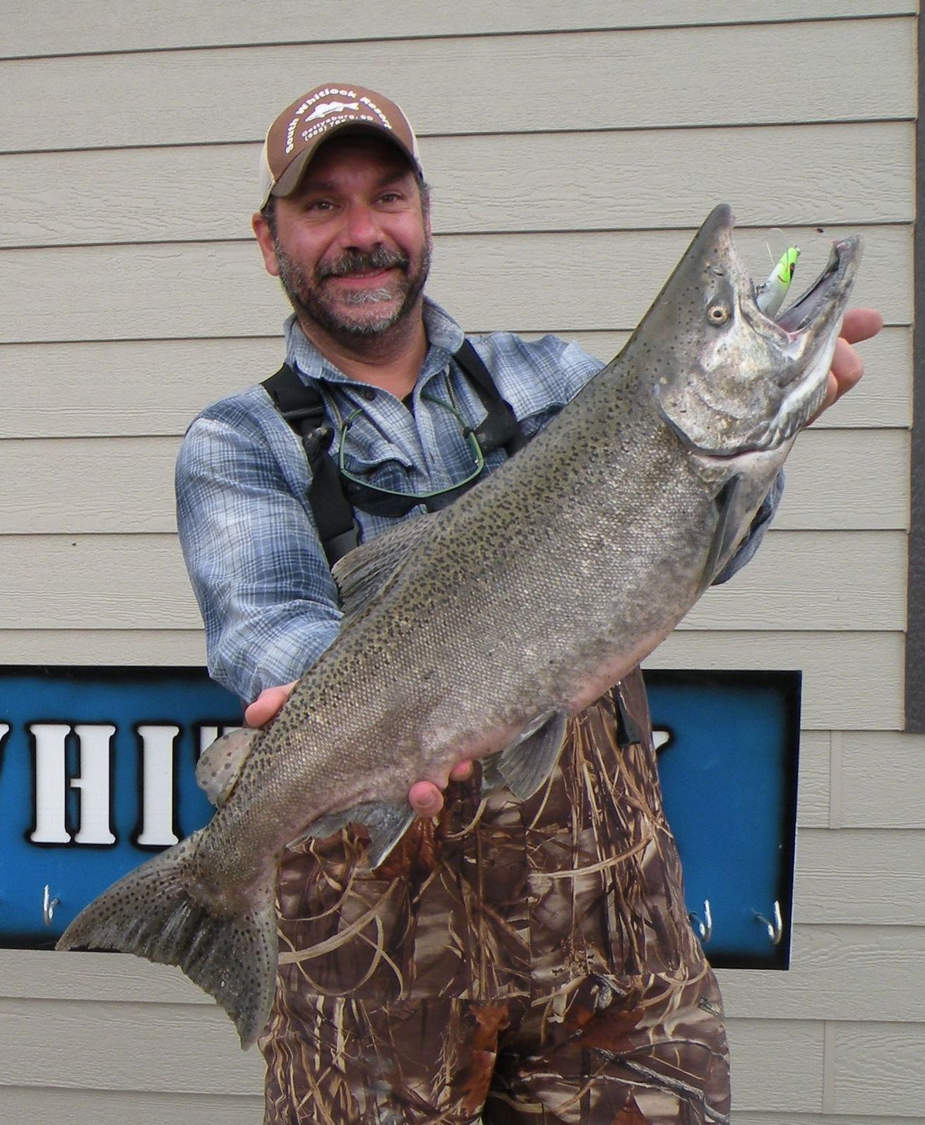 A man is holding a large fish in front of a sign that says hi