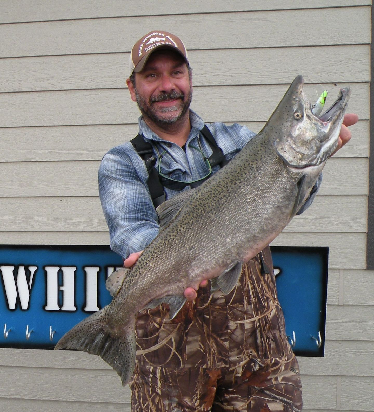 A man is holding a large fish in front of a sign that says whi