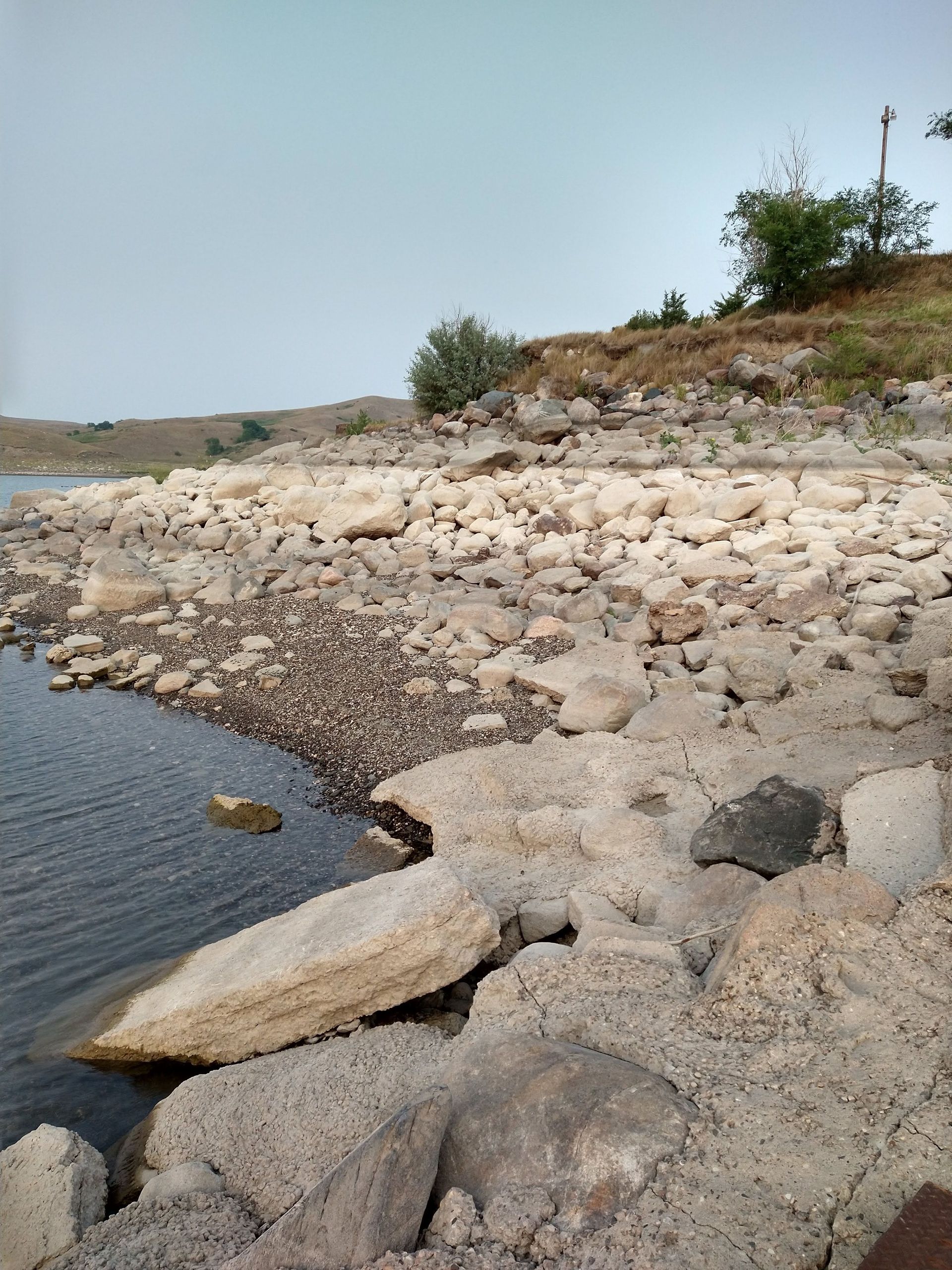 A large rock is sitting on the shore of a lake.