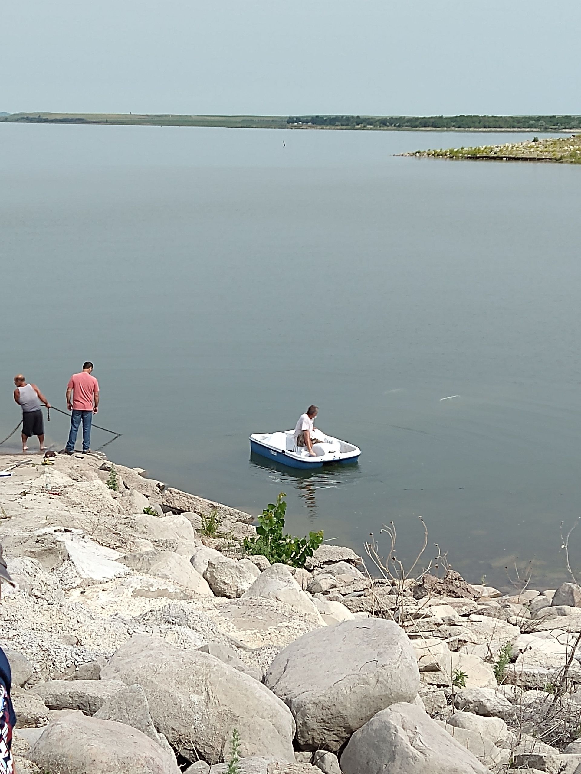 A group of people are standing on the shore of a lake with a boat in the water.