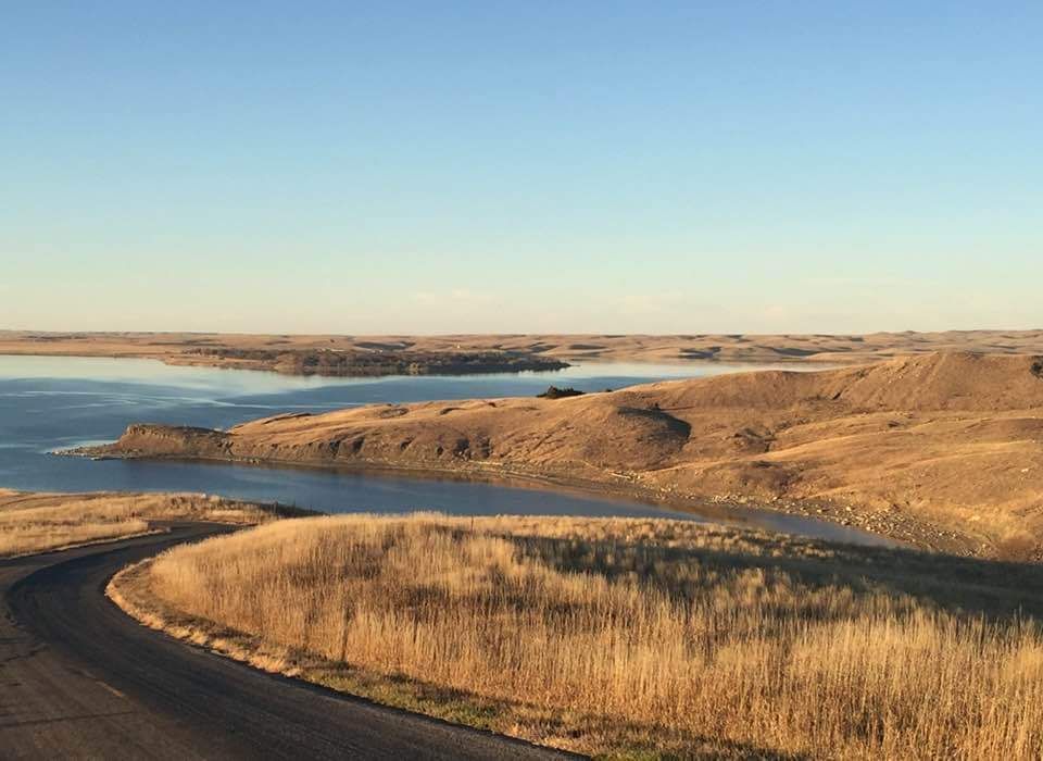 A road going through a desert landscape with a lake in the background.
