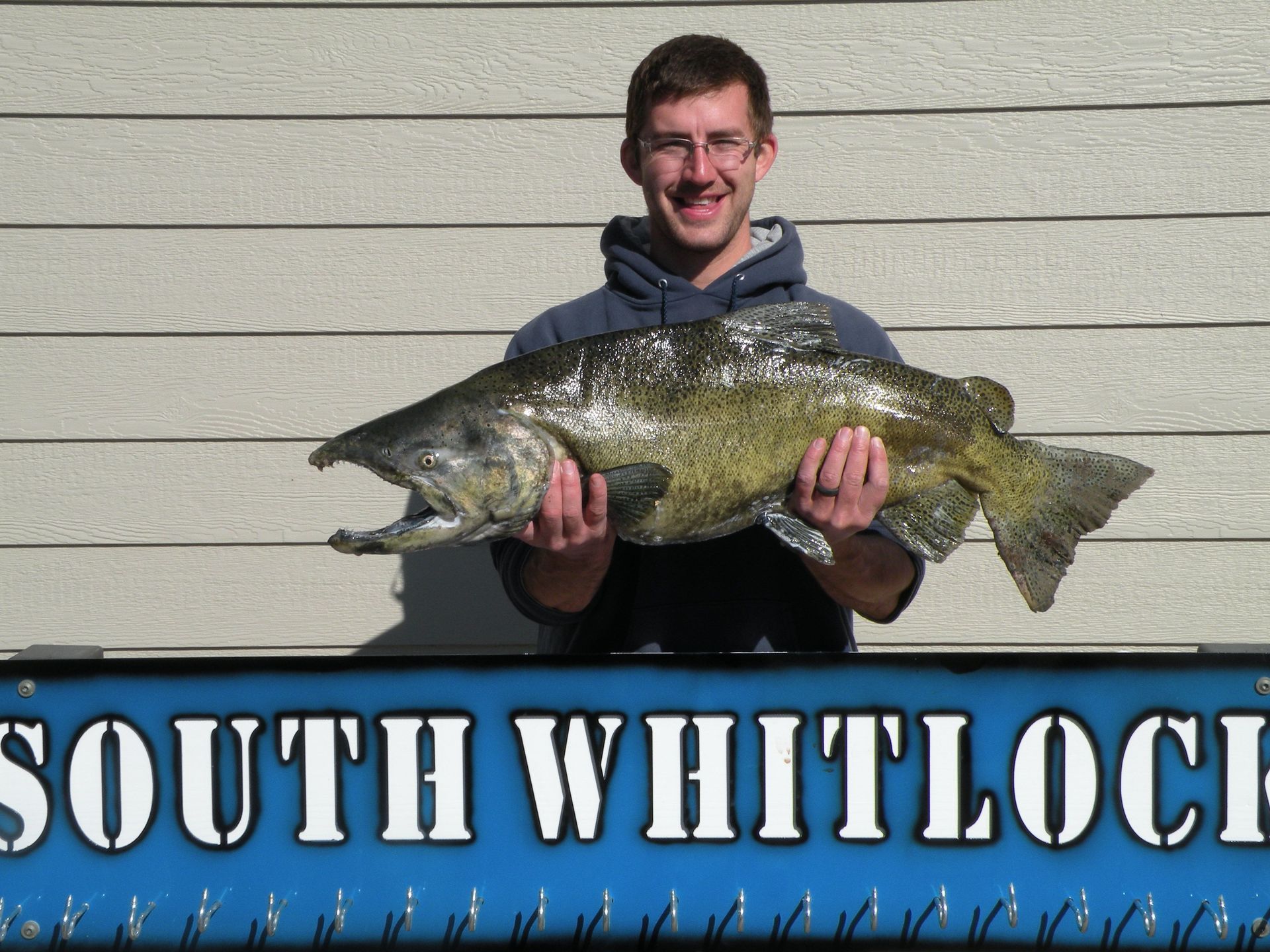 A man holding a large fish in front of a sign that says south whitlock