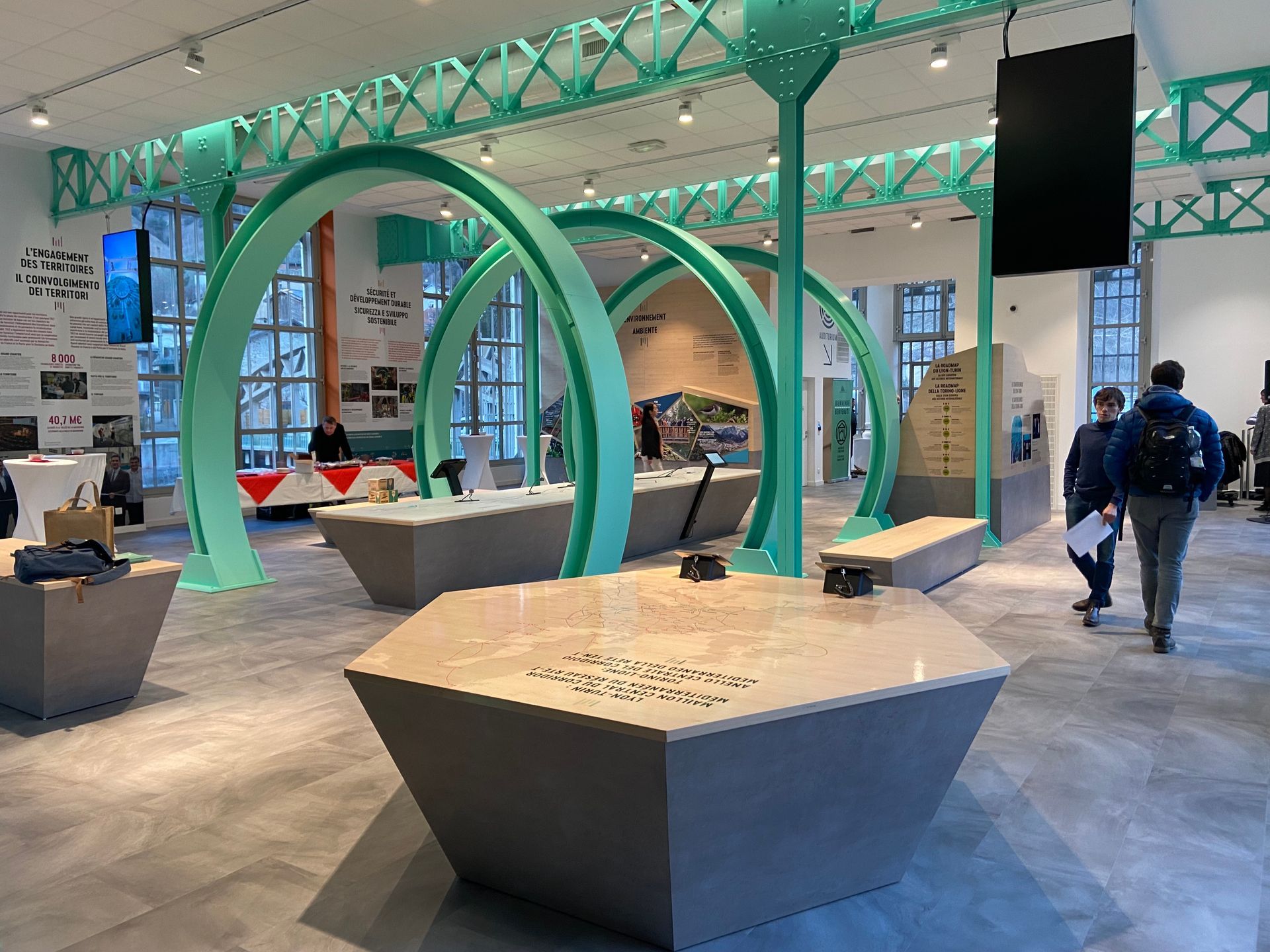 Exposition intérieure avec des arches circulaires turquoise, des tables hexagonales 