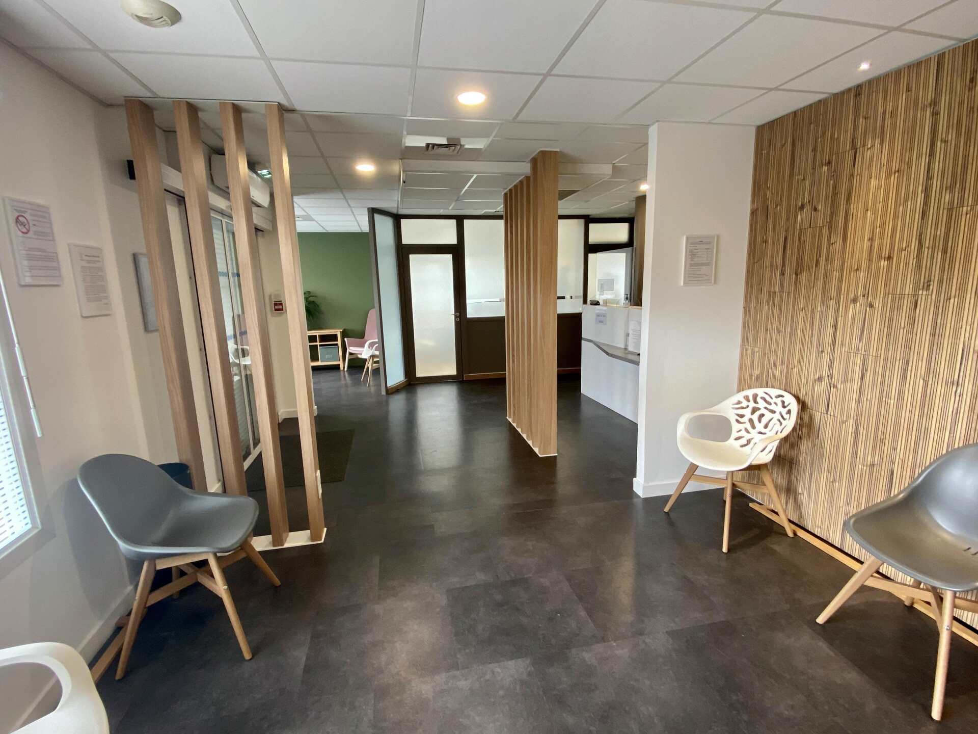 Salle d'attente moderne avec chaises, cloisons en bois, sol foncé et lambris tissé.