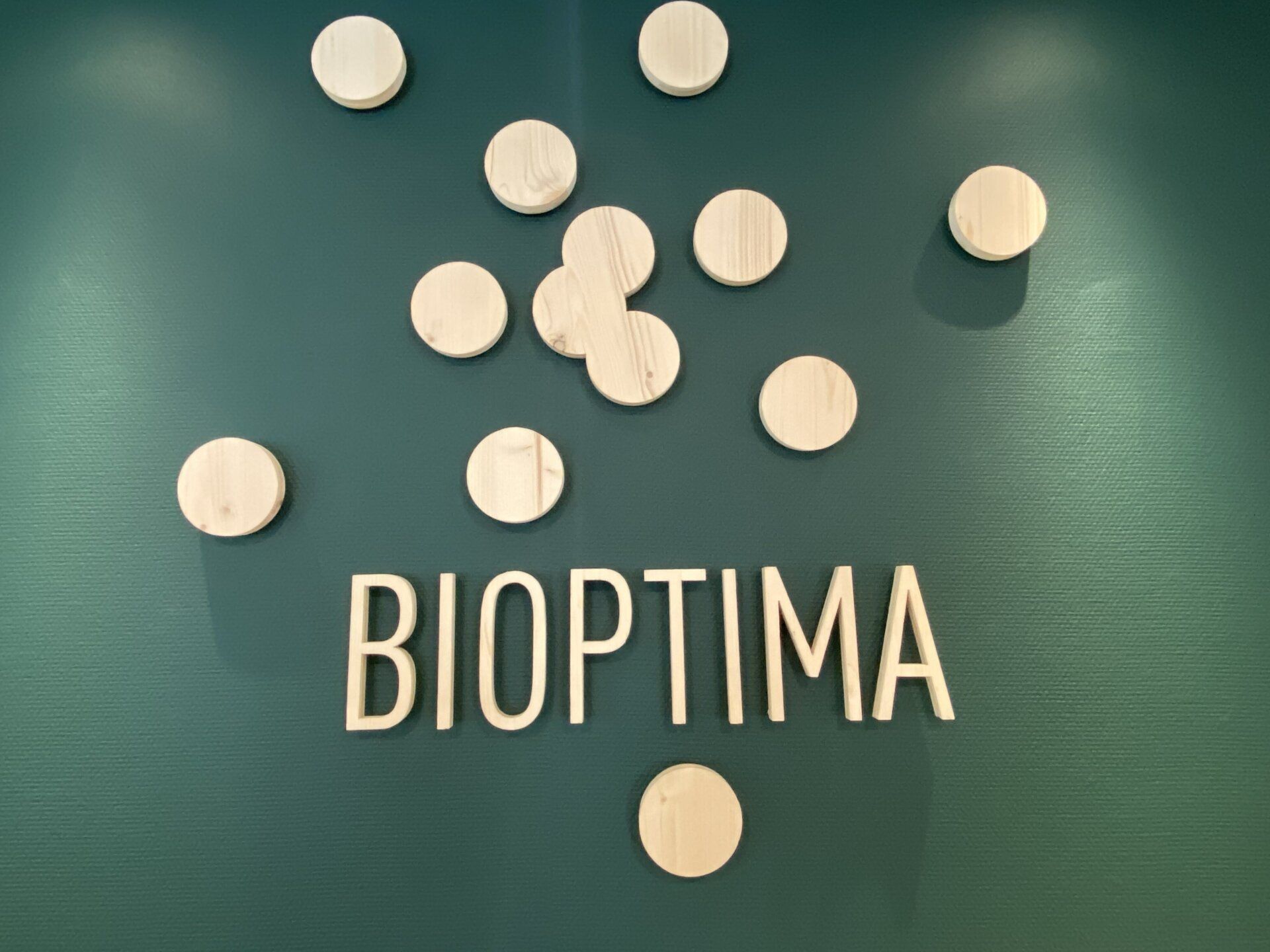 Des pilules blanches disposées au-dessus du mot « BIOPTIMA » sur fond vert