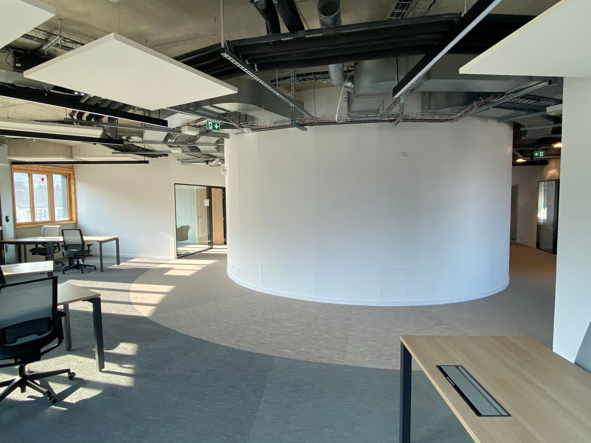 Intérieur de bureau ouvert avec un grand mur cylindrique blanc, des bureaux et un sol recouvert de moquette.