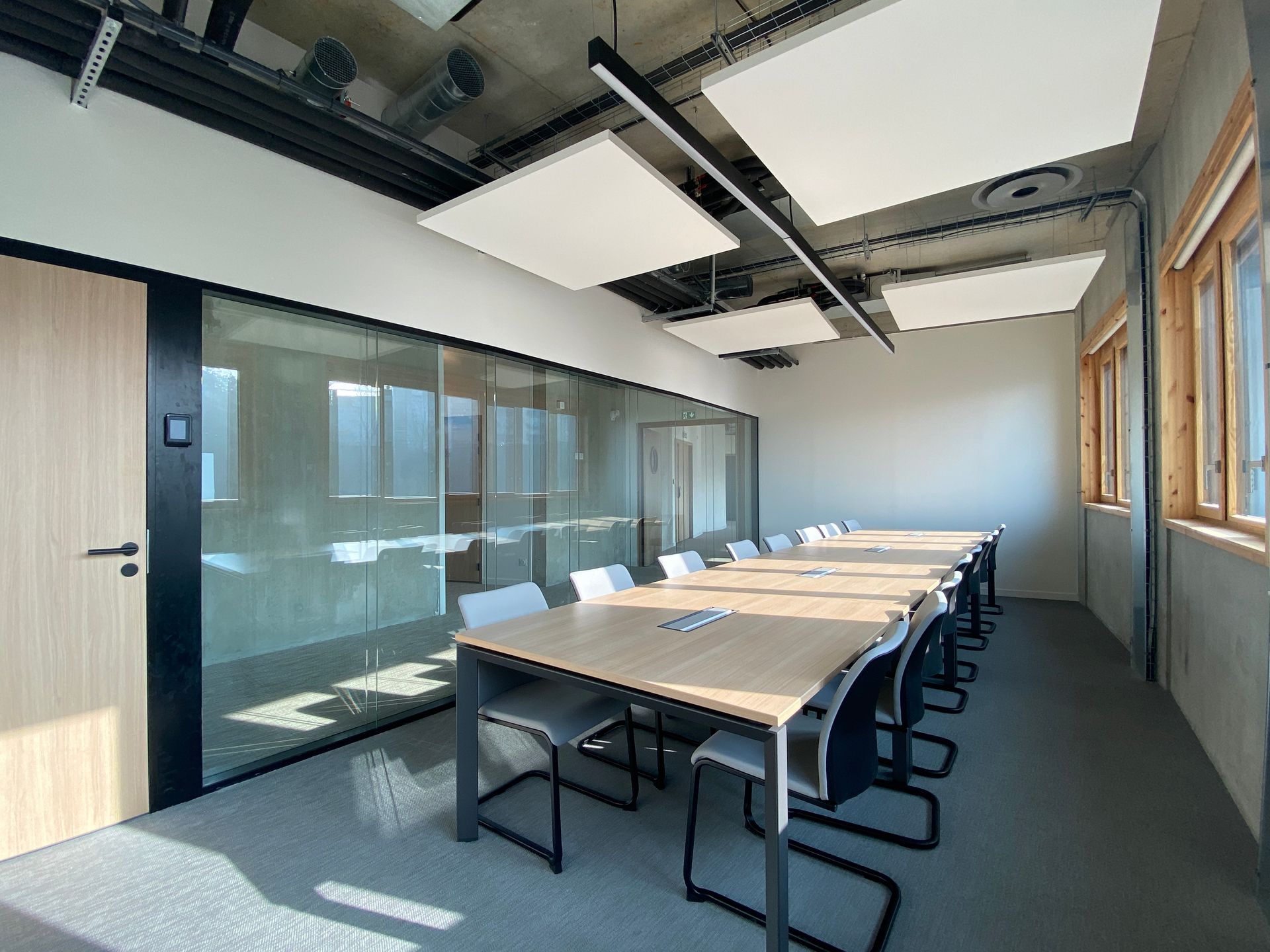 Salle de réunion moderne avec une longue table, des chaises noires, une paroi vitrée et de grandes fenêtres 