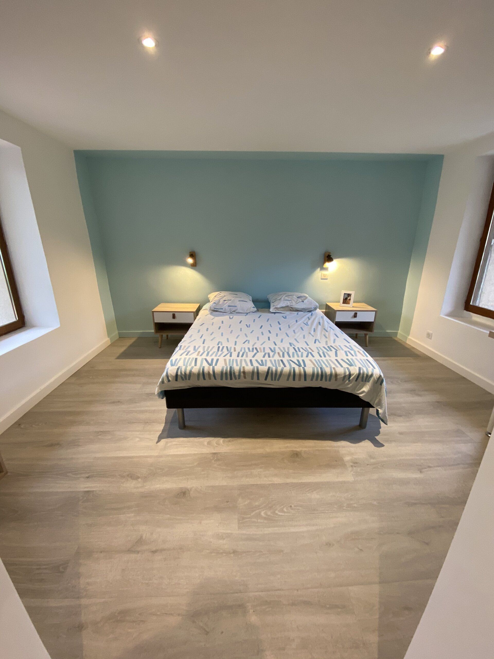 Chambre d'amis avec un lit centré contre un mur bleu et deux lampes de chevet.