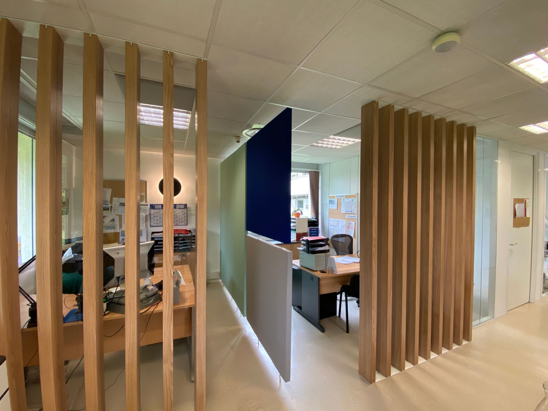 Couloir de bureau moderne avec cloisons à lattes de bois et espaces de travail visibles au-delà.