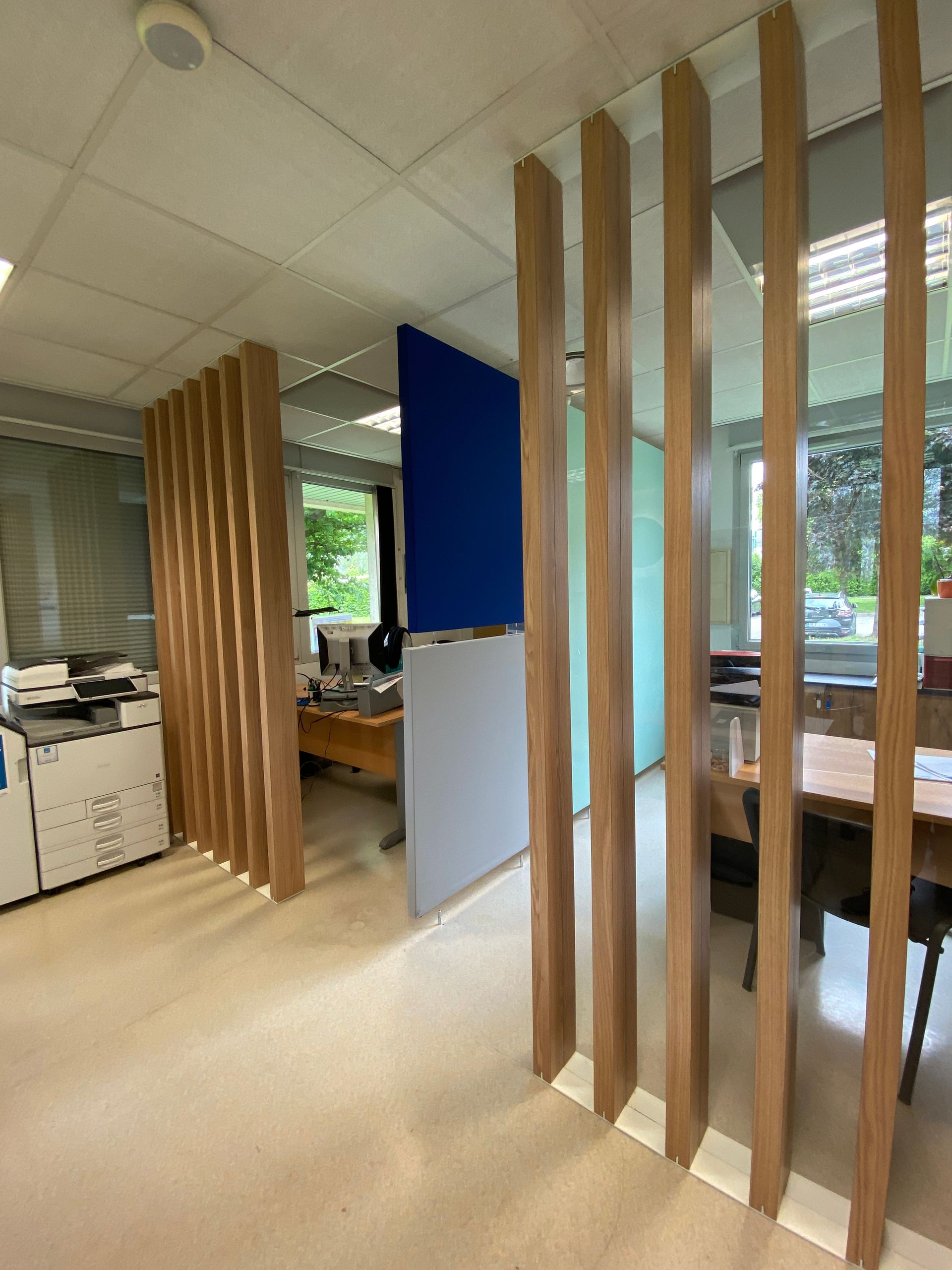 Intérieur de bureau moderne avec cloisons en lattes de bois, bureaux et grandes fenêtres donnant sur la verdure.