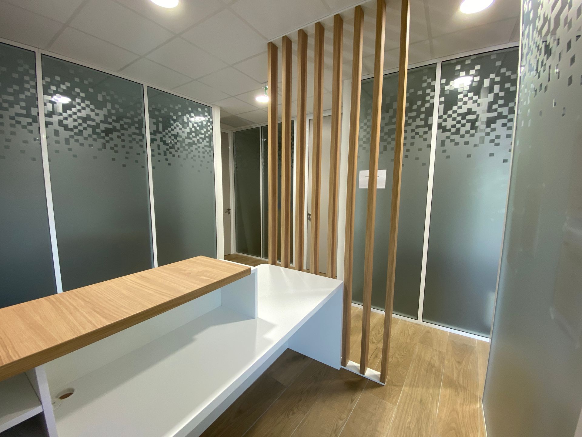 Espace d'accueil moderne avec parois en verre dépoli, cloison en lattes de bois et comptoir d'accueil blanc et bois.