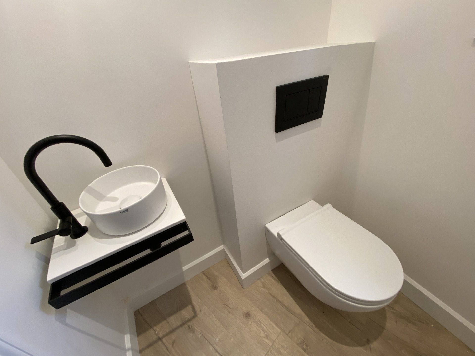 Petite salle de bains moderne avec toilettes suspendues, lavabo et robinet noir sur un meuble-lavabo compact.