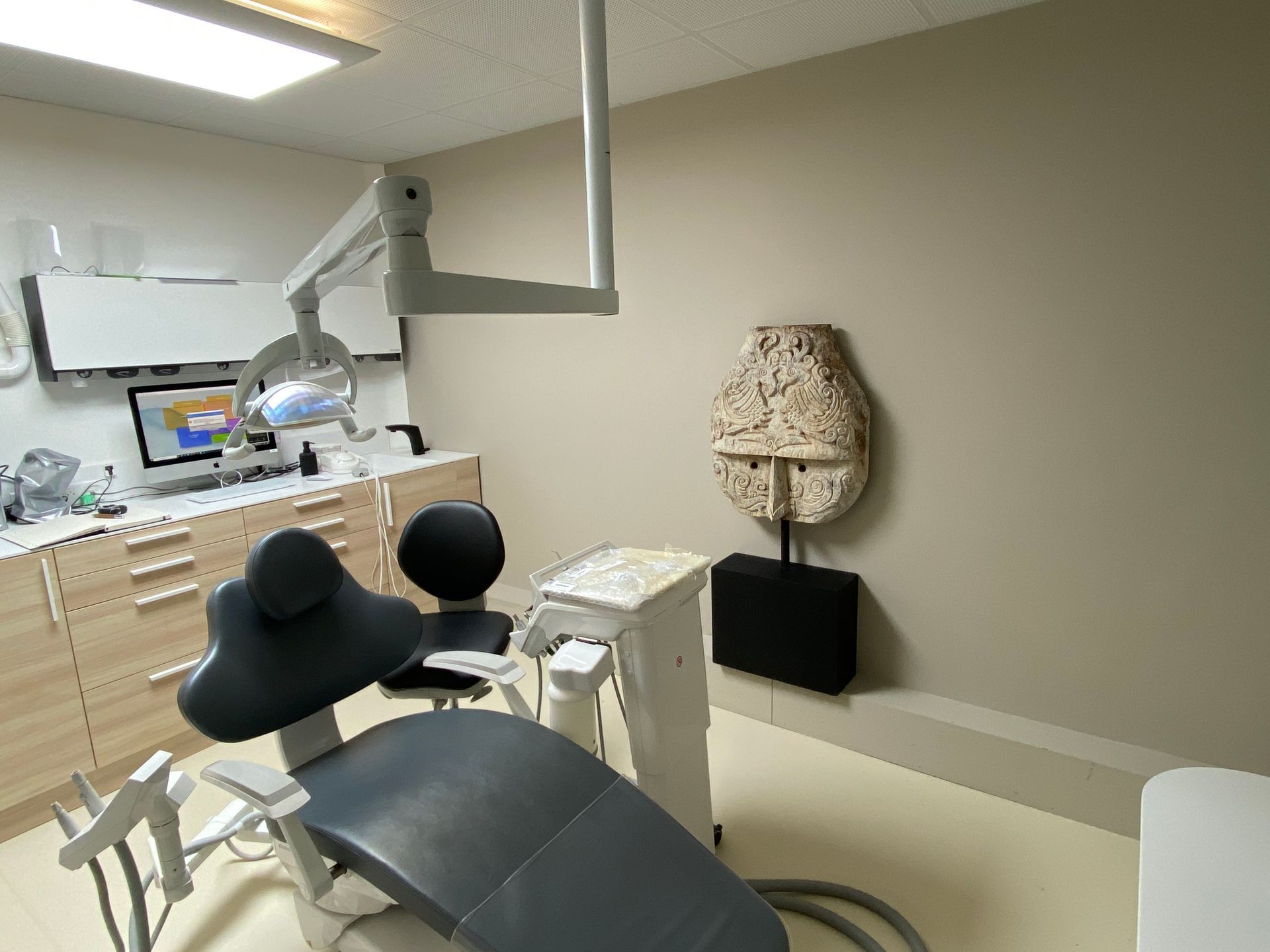 Salle d'examen dentaire avec fauteuil, éclairage au plafond, armoires et lampe décorative