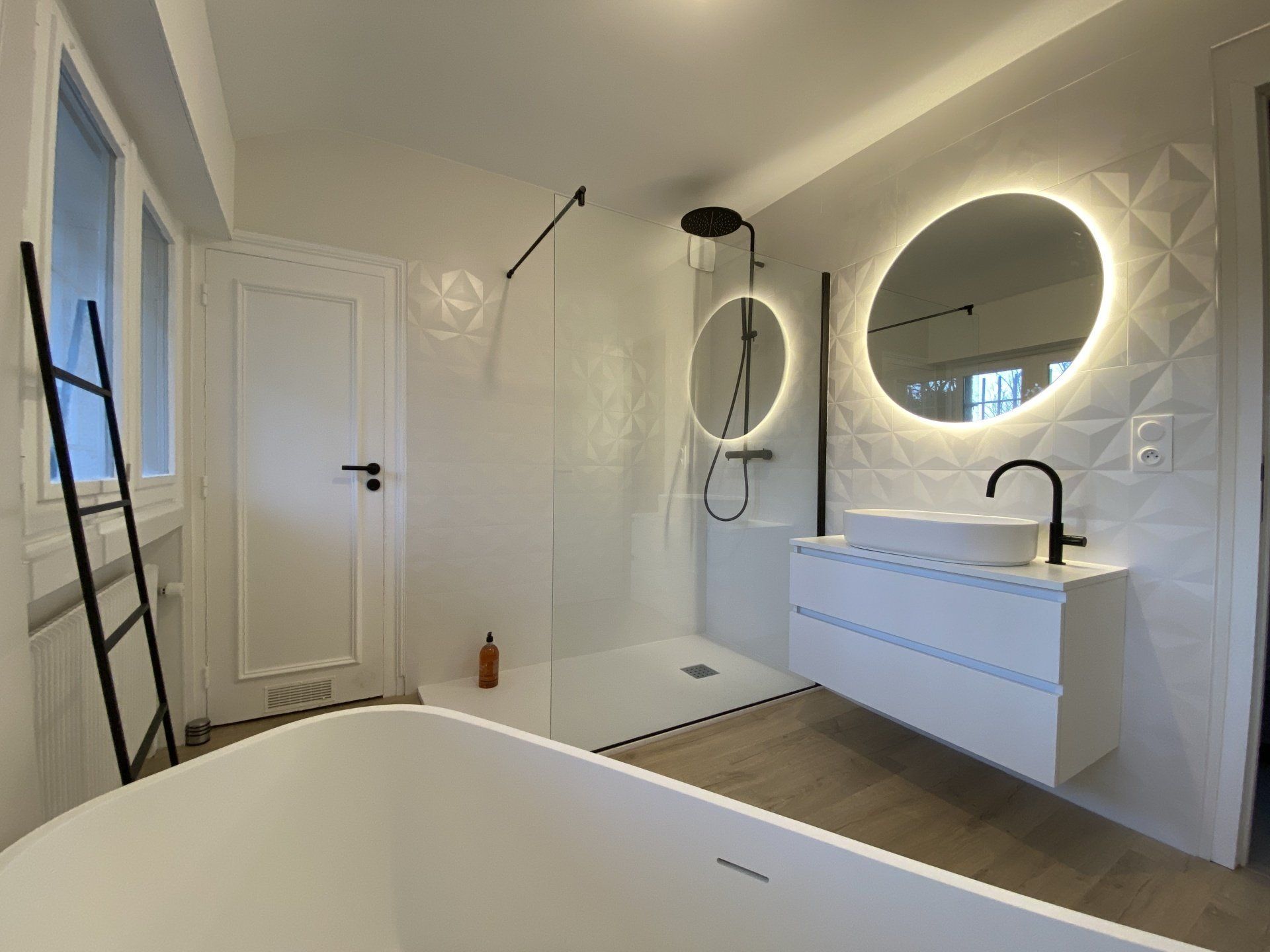 Salle de bains moderne blanche avec baignoire îlot, douche à l'italienne, meuble-lavabo et miroir rond éclairé