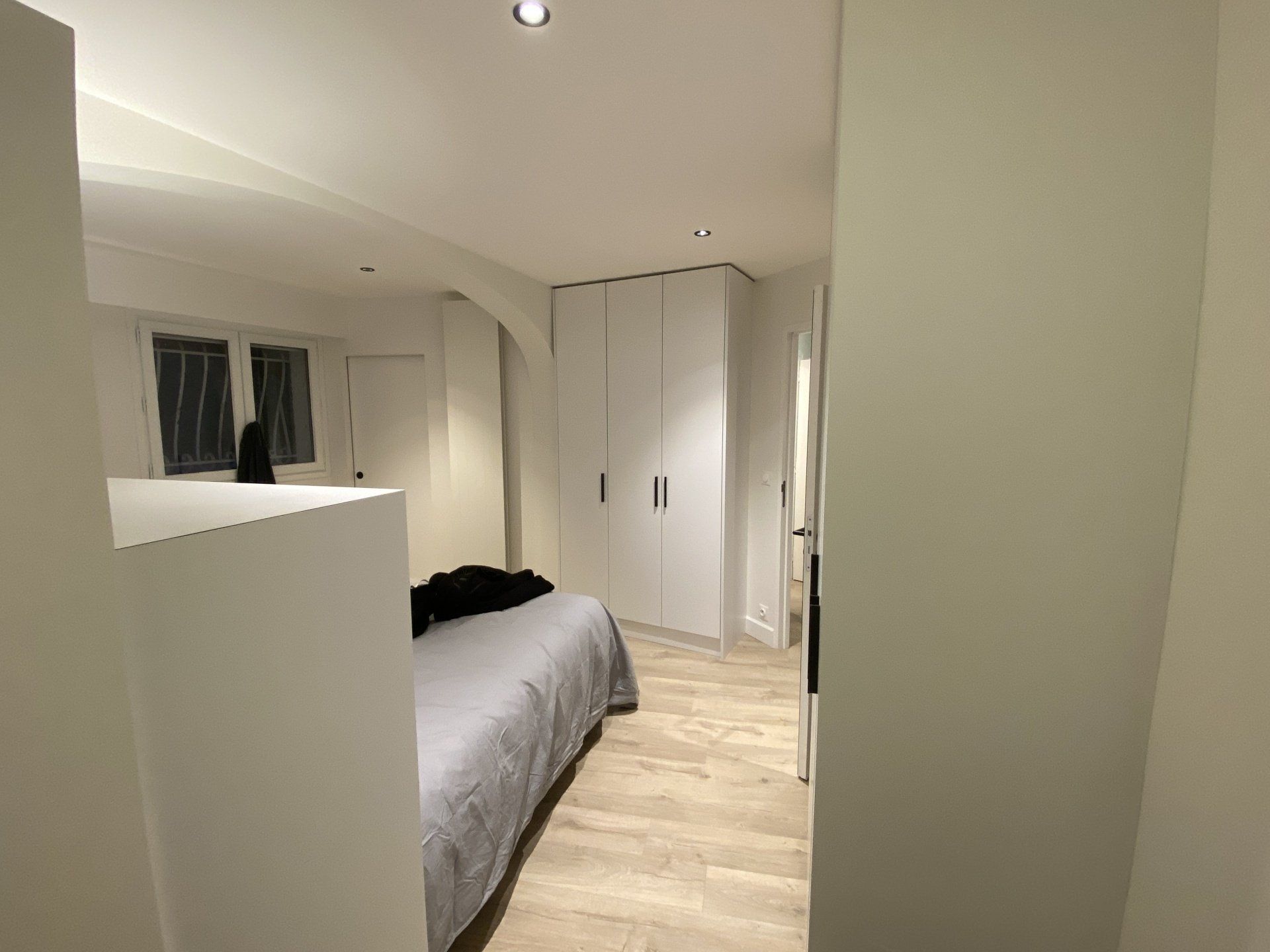 Petite chambre avec un lit, des armoires blanches et un parquet clair.