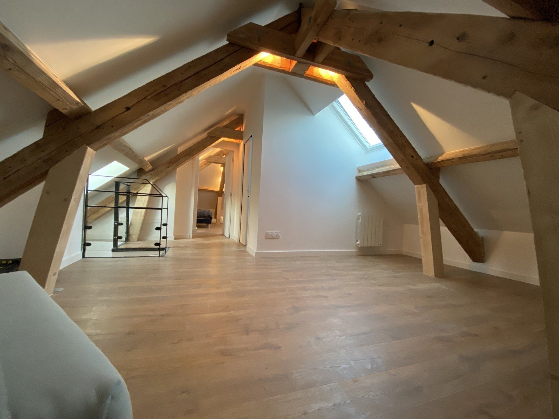 Grenier vide avec poutres apparentes, plafond mansardé et parquet clair