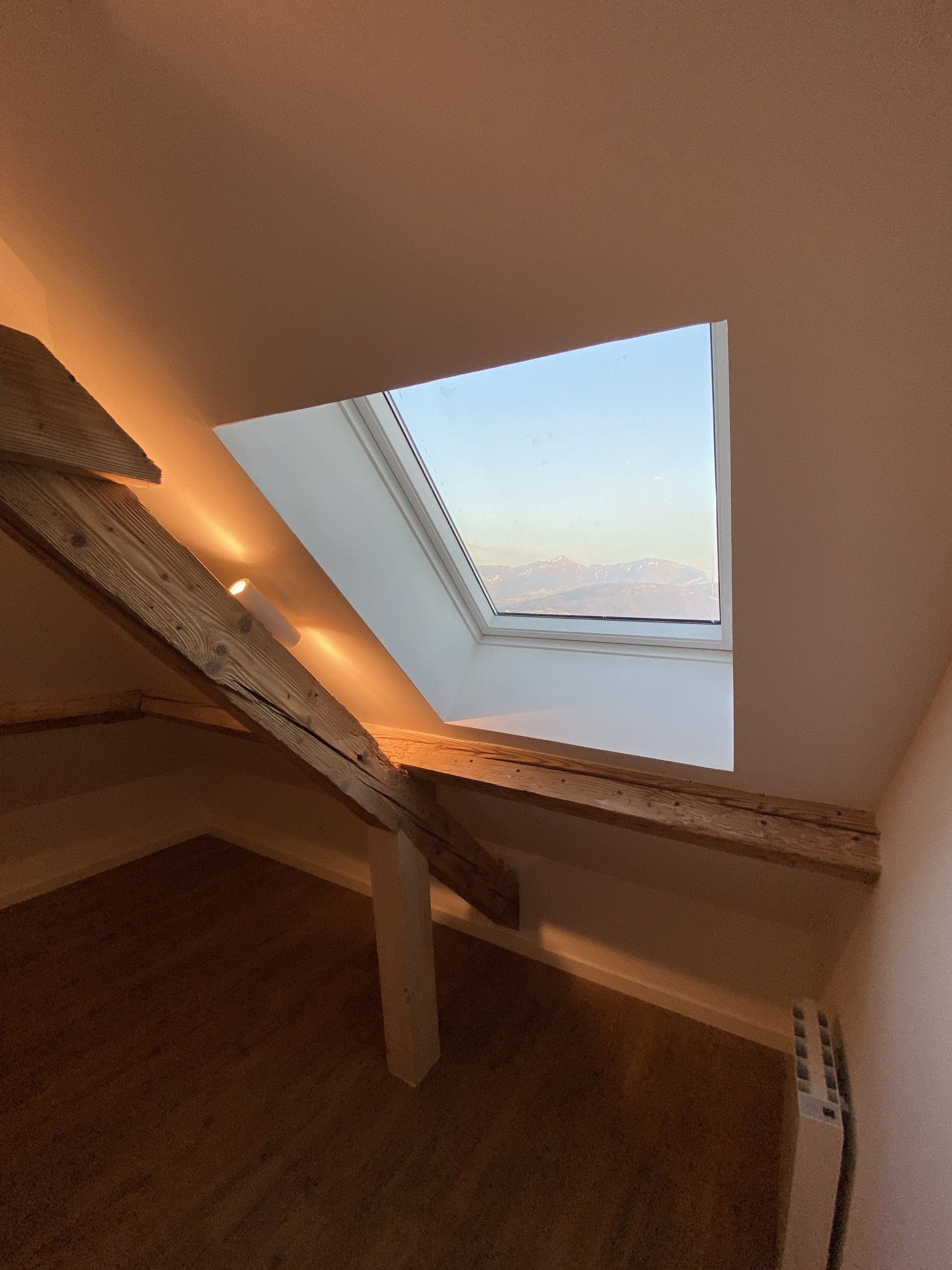 Pièce mansardée avec plafond en pente, fenêtre de toit et éclairage encastré chaleureux au-dessus d'un parquet.