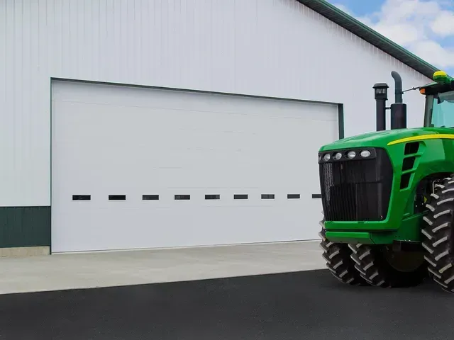 A large white garage door next to a green John Deere tractor on a concrete pad.