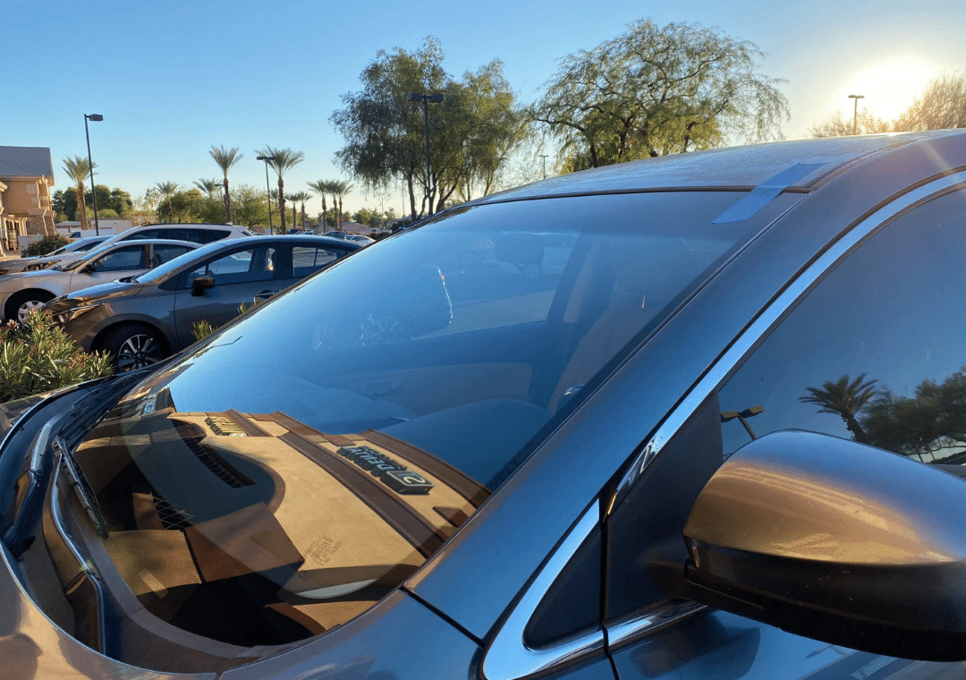 A car is parked in a parking lot with the sun shining through the windshield.