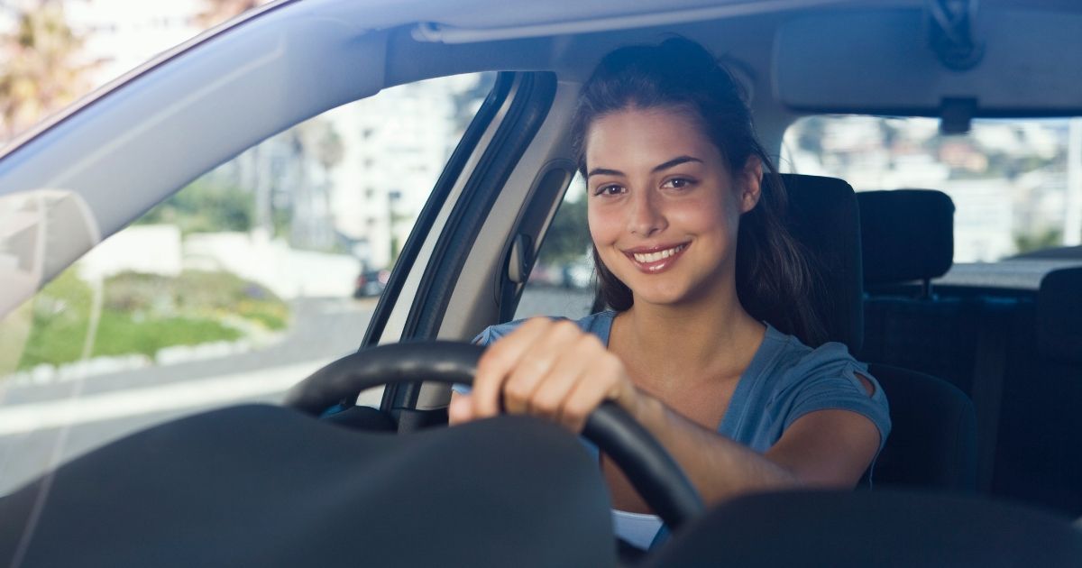 A woman is driving a car and smiling at the camera.