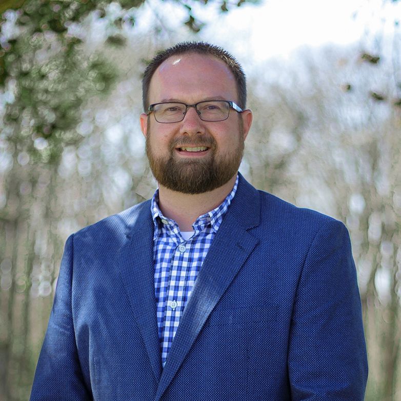 A man with a beard and glasses is wearing a blue suit and a plaid shirt.