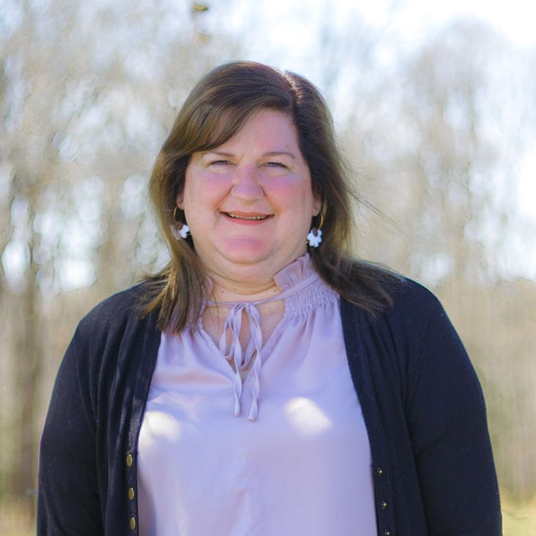 A woman in a purple shirt and black cardigan is smiling for the camera.