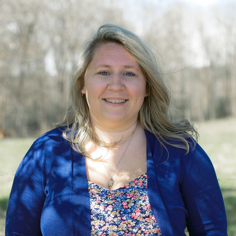 A woman wearing a blue cardigan and a floral top smiles for the camera