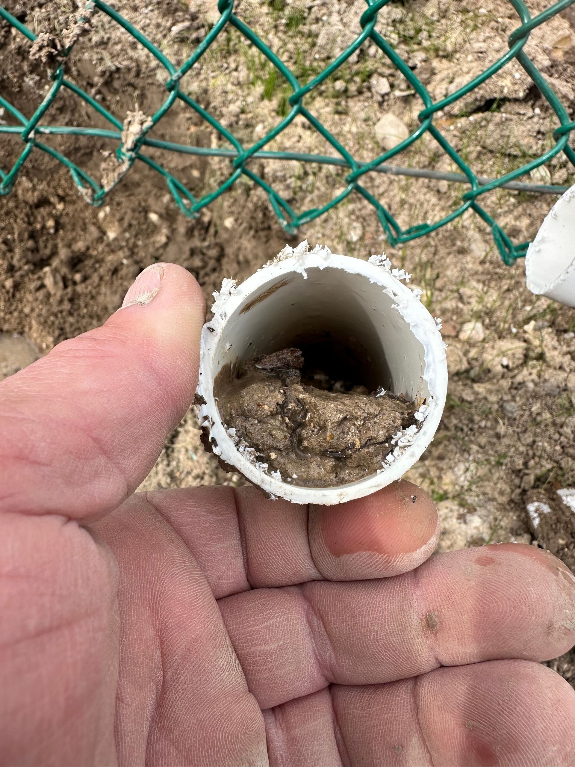 A person is holding a dirty pipe in their hand in front of a chain link fence.