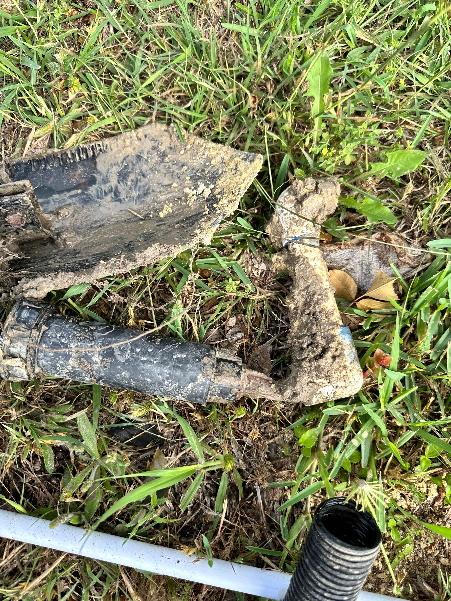 A shovel is laying on the grass next to a pipe.