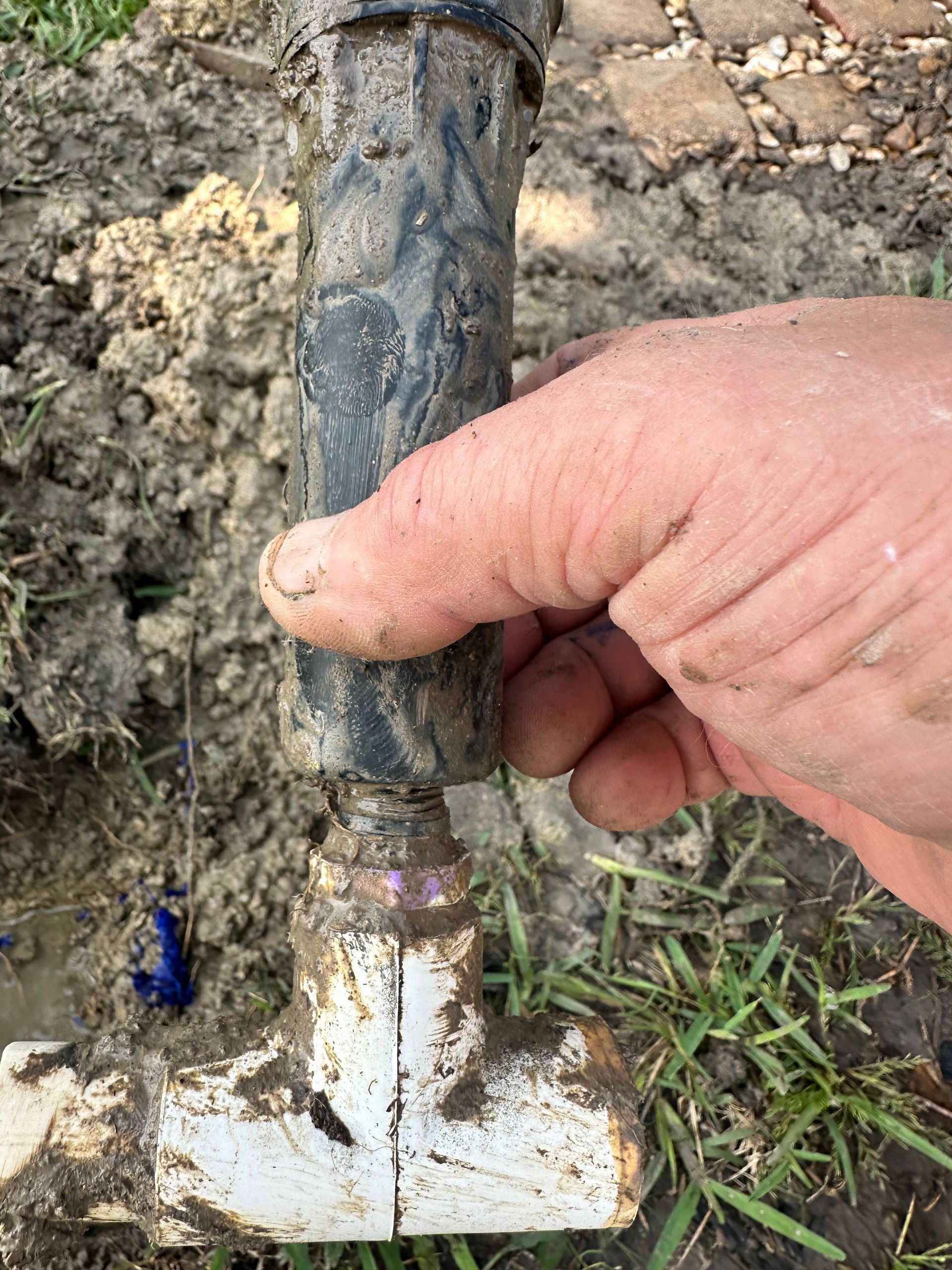 A person is holding a muddy pipe in their hand.