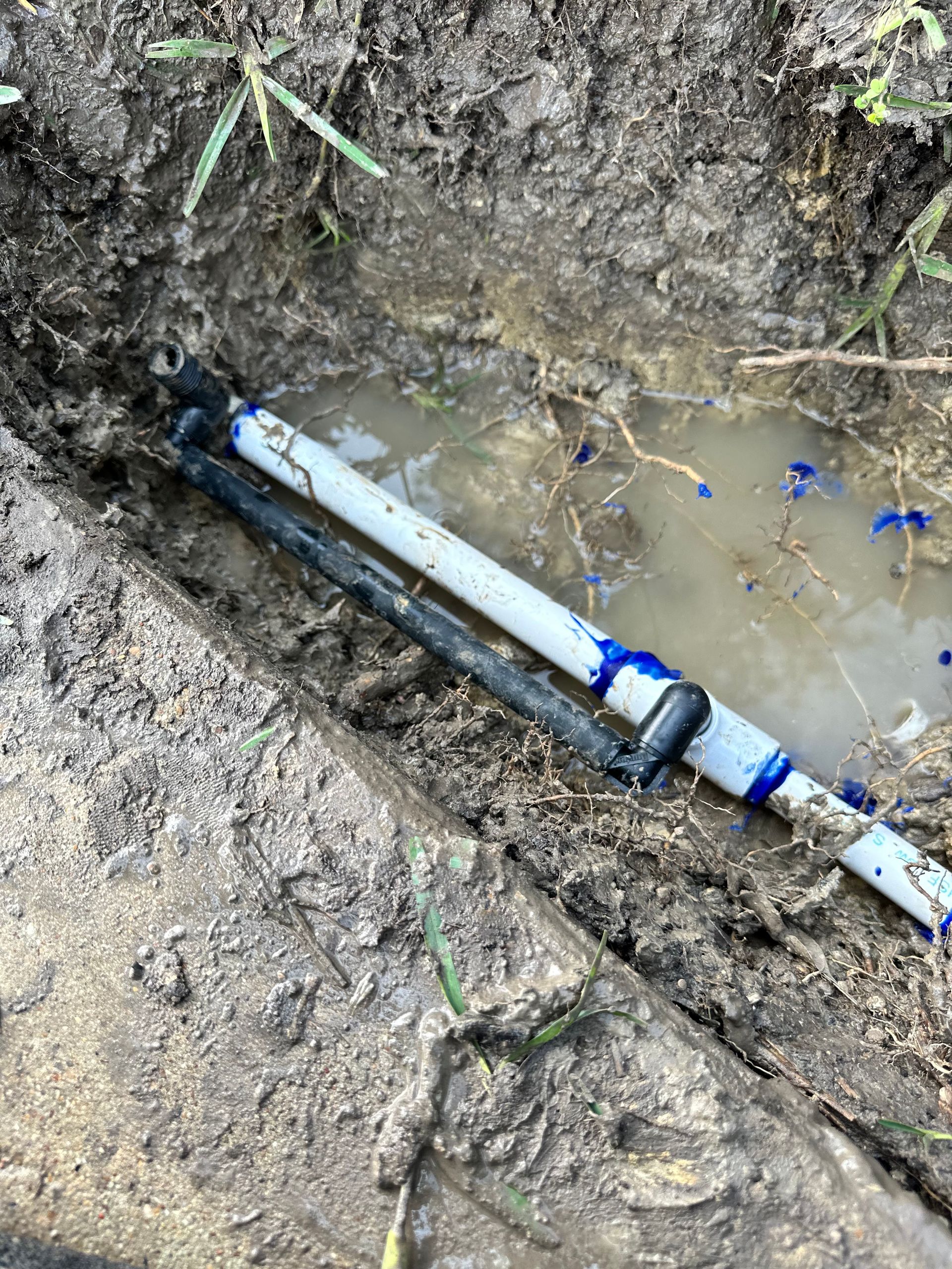 A white pipe is laying in the dirt next to a drain.
